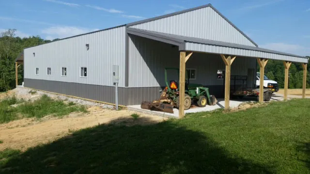 White machine shed set into a bank with a timber-post open shed and a tractor parked under it