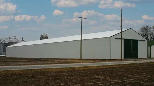 Long white machine shed with green sliding doors standing beside grain bins