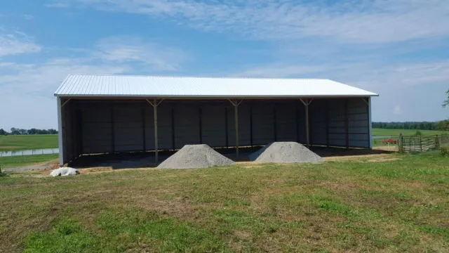 Open-front pole shed with a white roof, aggregate stored in the bays