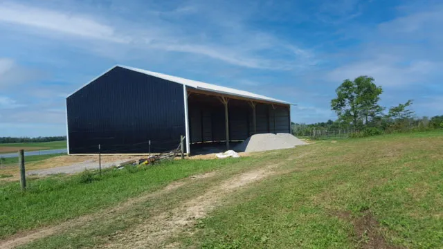 Dark navy open-front shed with a white roof standing beside a pond