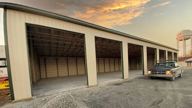 Long open-sided storage building on timber posts with a pickup outside and a water tower behind