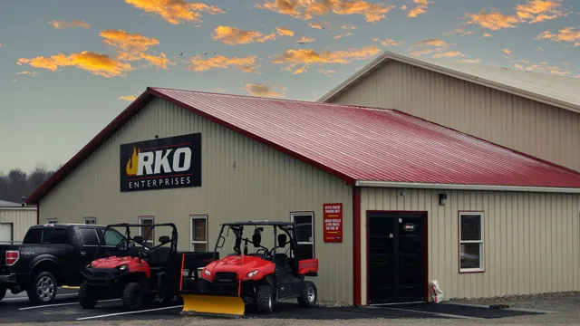 Tan commercial building with a red roof and signage, vehicles parked outside