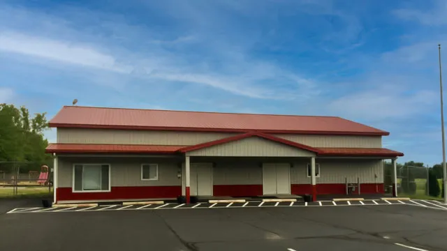 Cream commercial building with a red roof and red wainscot on a paved lot