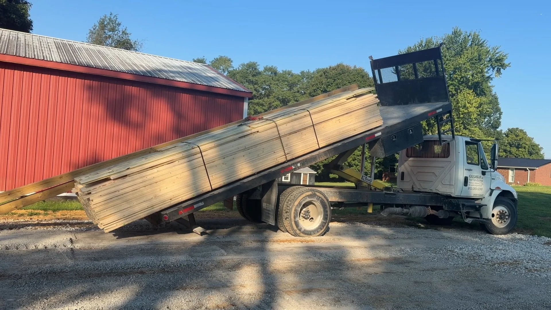 Gosman truck tilting its bed to unload a bundled kit package at a red building