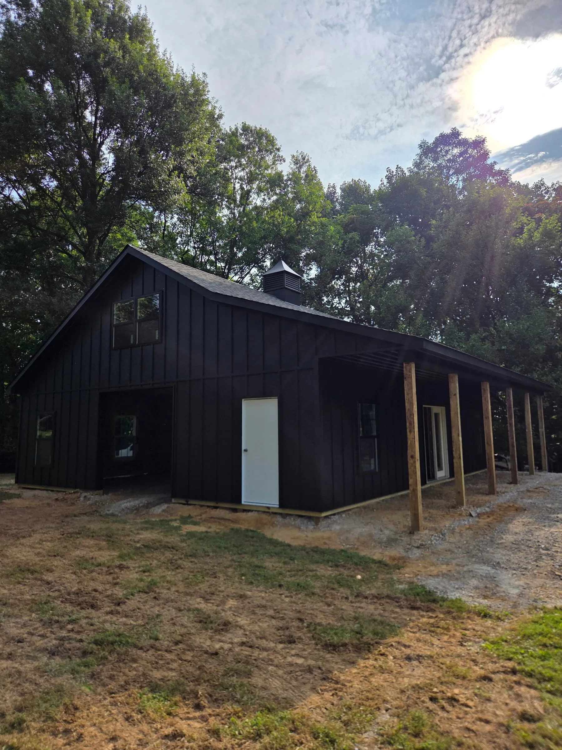 Black board and batten building with a long open pole shed along the side