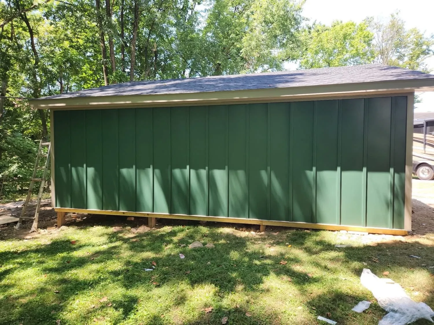 Green board and batten shed with a gray metal roof on a mowed lawn