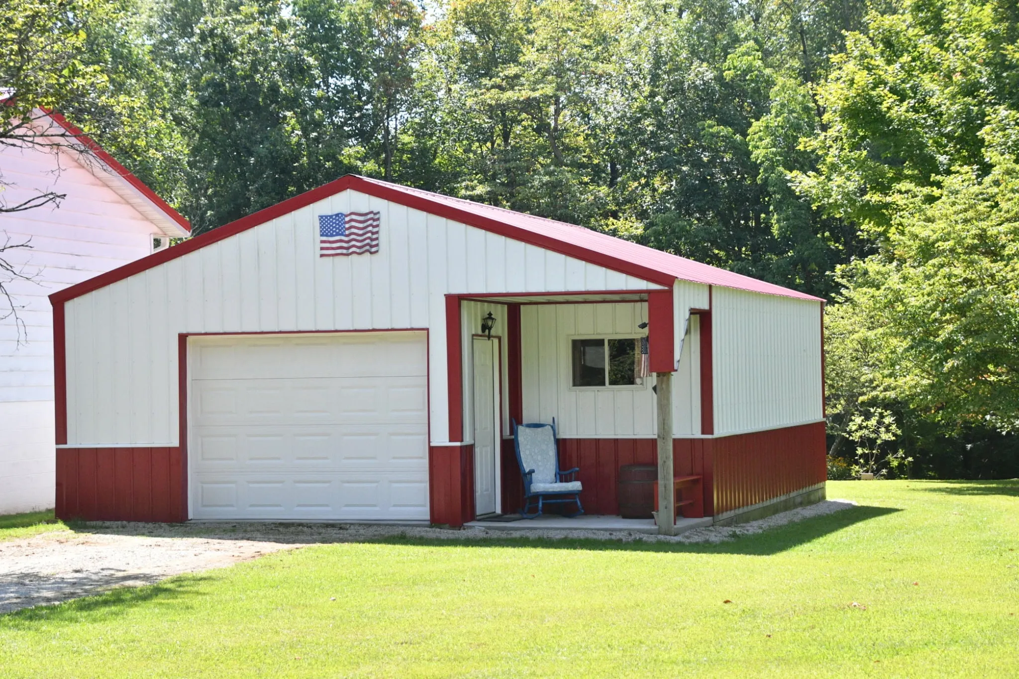 White garage with a red roof and red trim, an inset porch beside the overhead door and an American flag on the gable