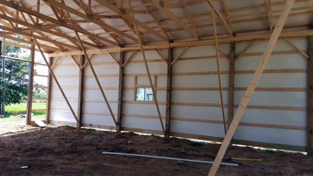 Inside a post frame shell with white lined walls and open trusses overhead