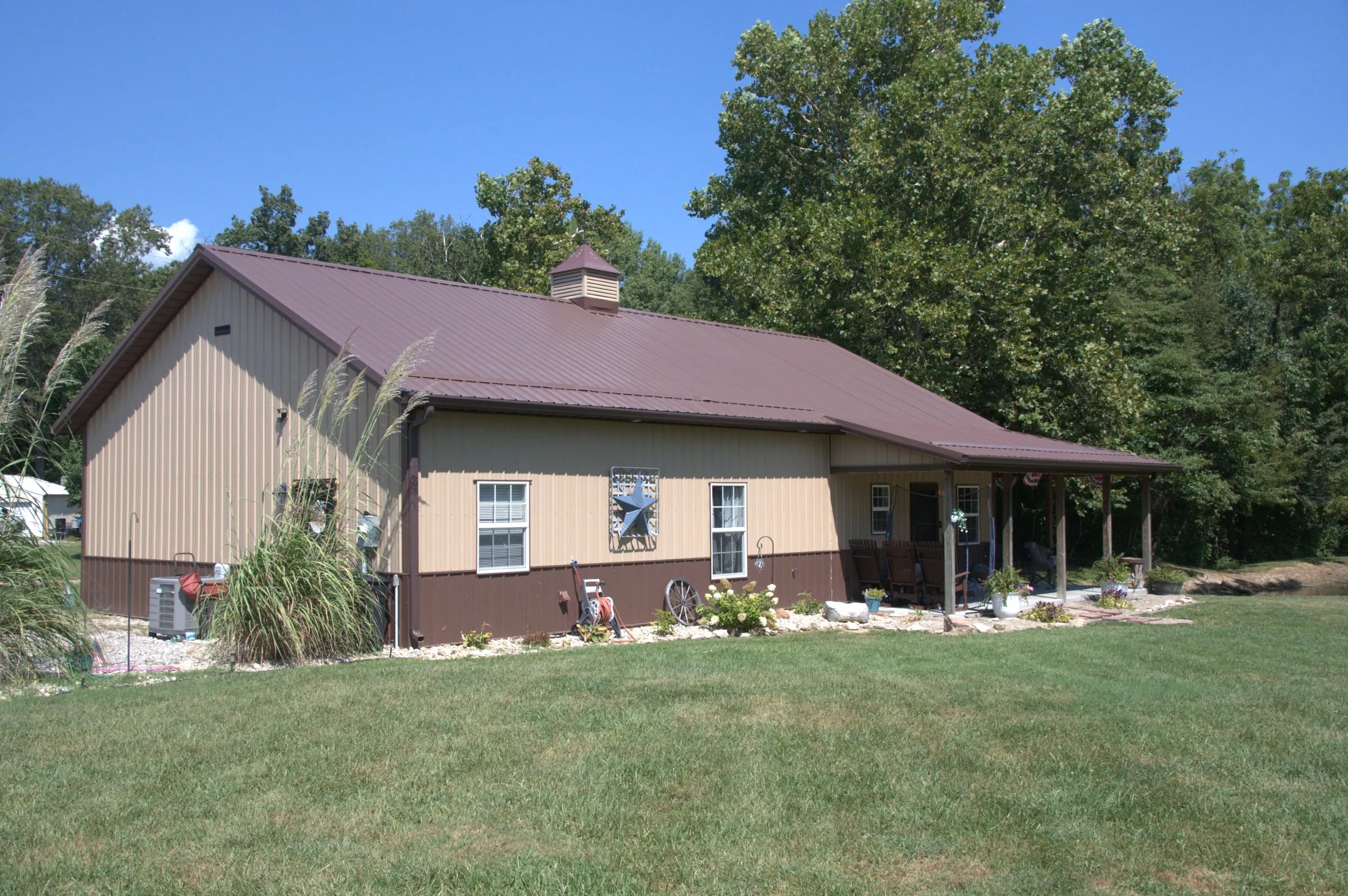 Tan house-style building with a maroon roof and a lean-to porch along the side, with landscaping and a cupola