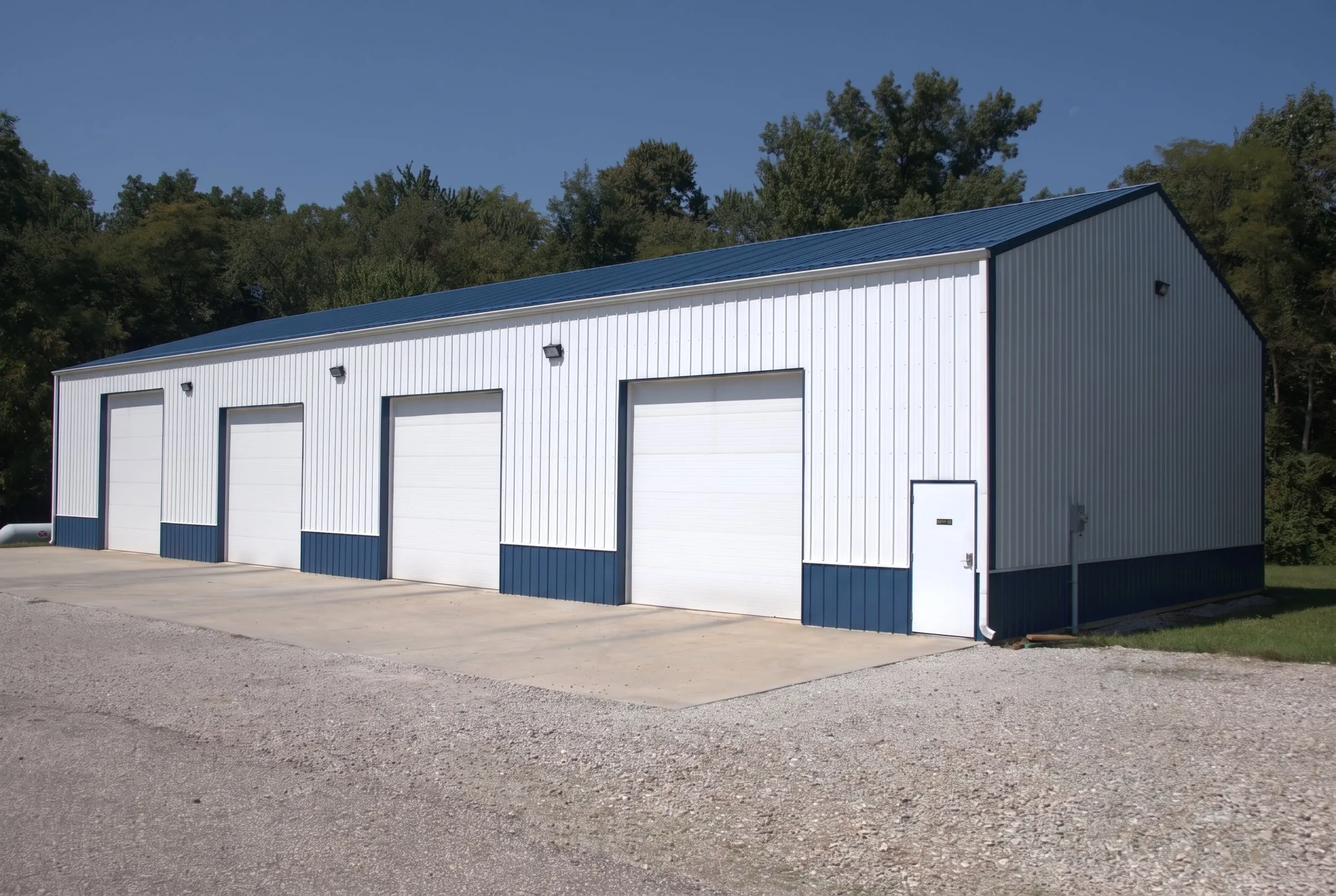 White shop with a blue roof and blue wainscot, four white overhead doors and a walk door on a concrete apron