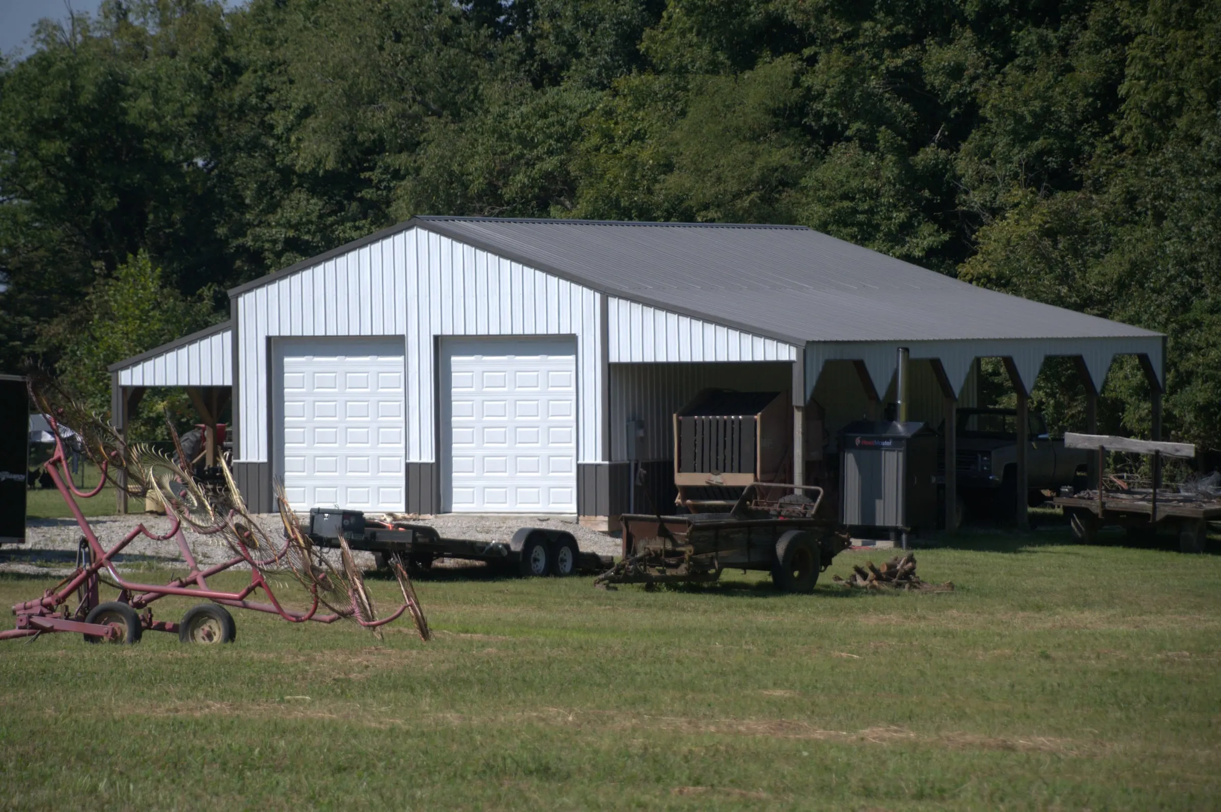 White shop with two overhead doors and an open shed porch on the end, with farm equipment parked outside