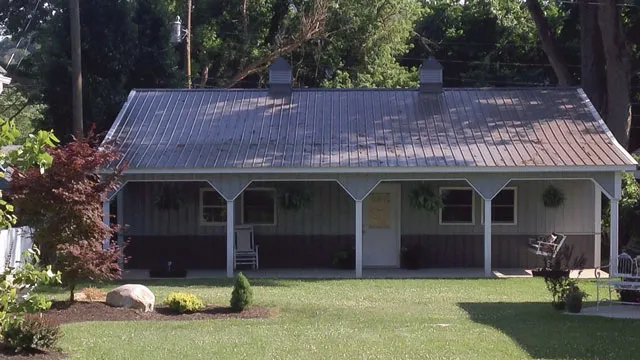 Gray building with a dark roof, a full-length porch and planted beds along the front