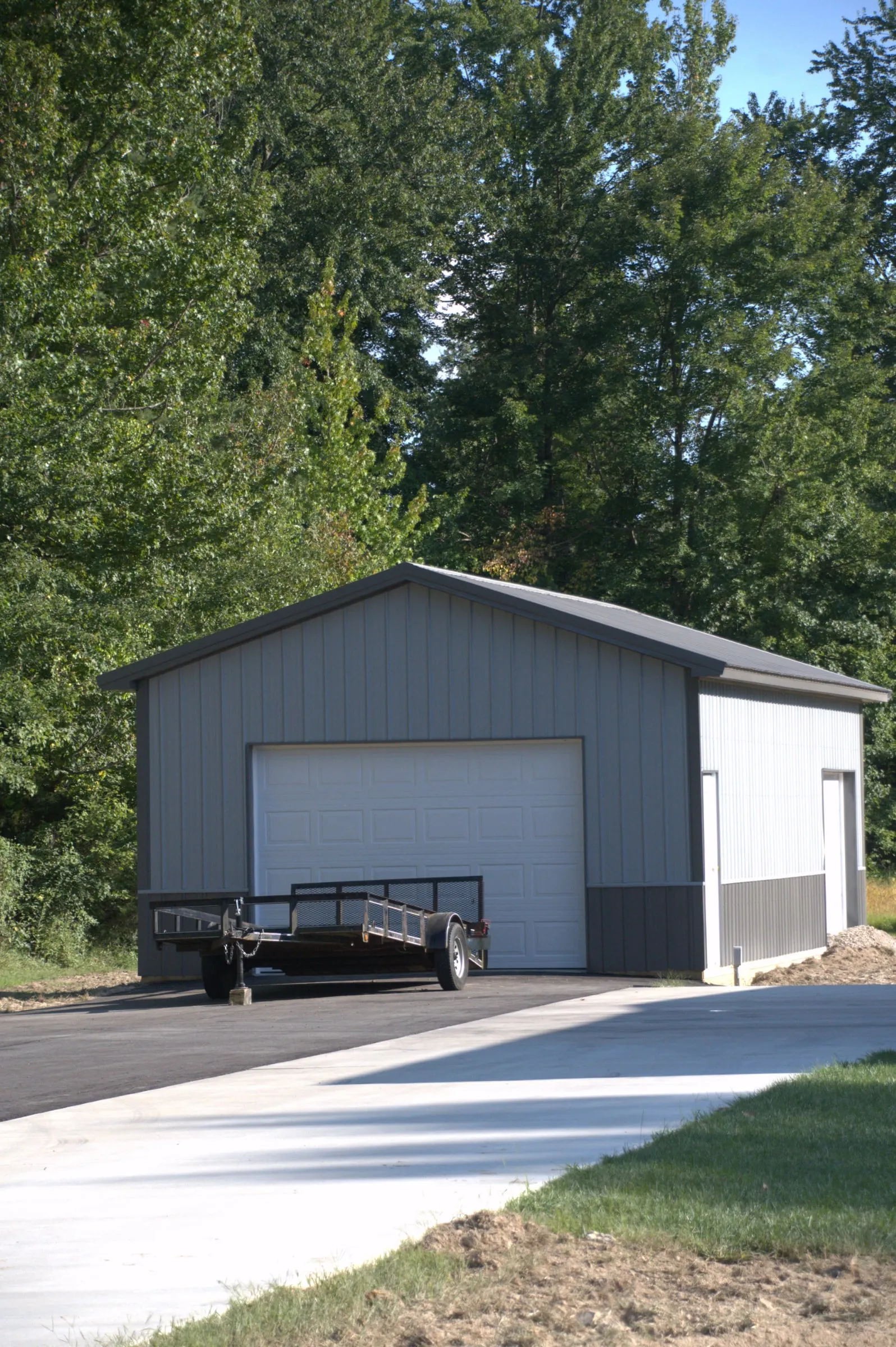 Small tan garage with one white overhead door and a walk door at the end of a new concrete drive