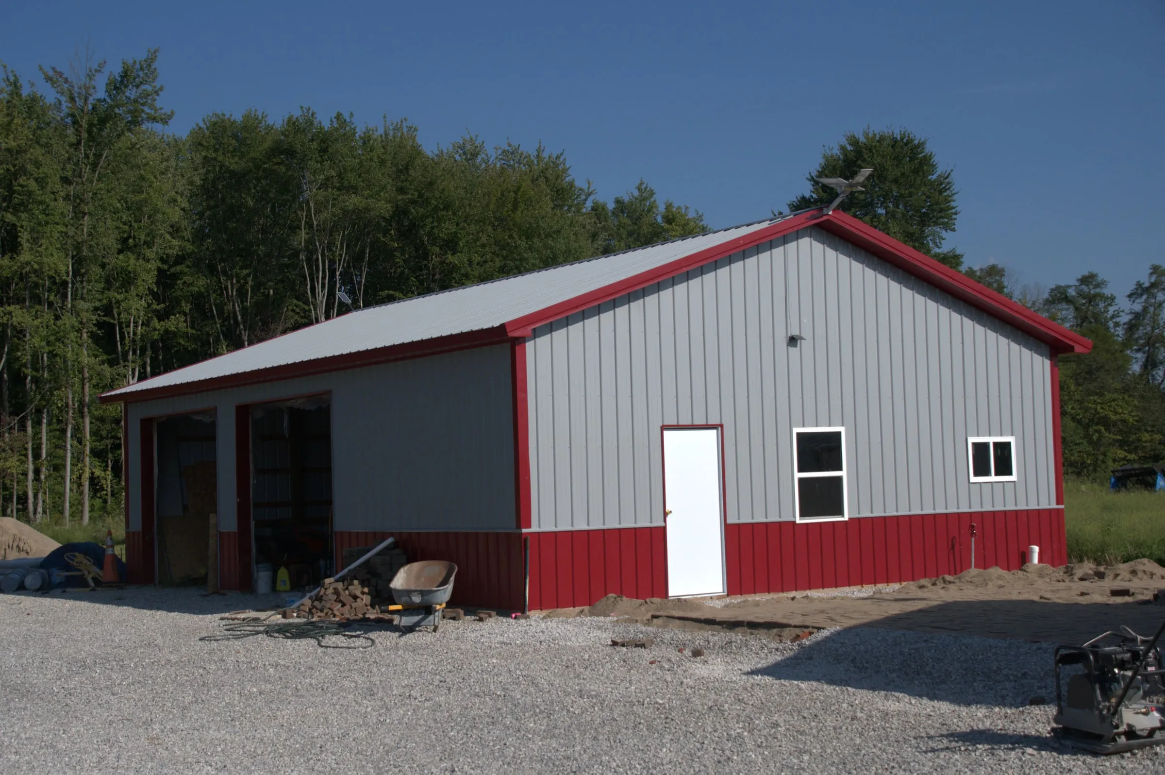 Gray shop with a red roof, red trim and red wainscot, a white walk door, window and overhead door