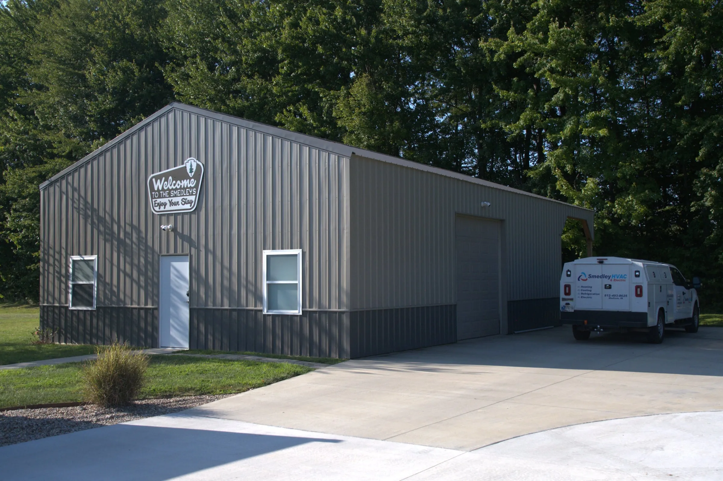 Gray shop with charcoal wainscot, a white walk door and a tall overhead door on the end, van parked outside