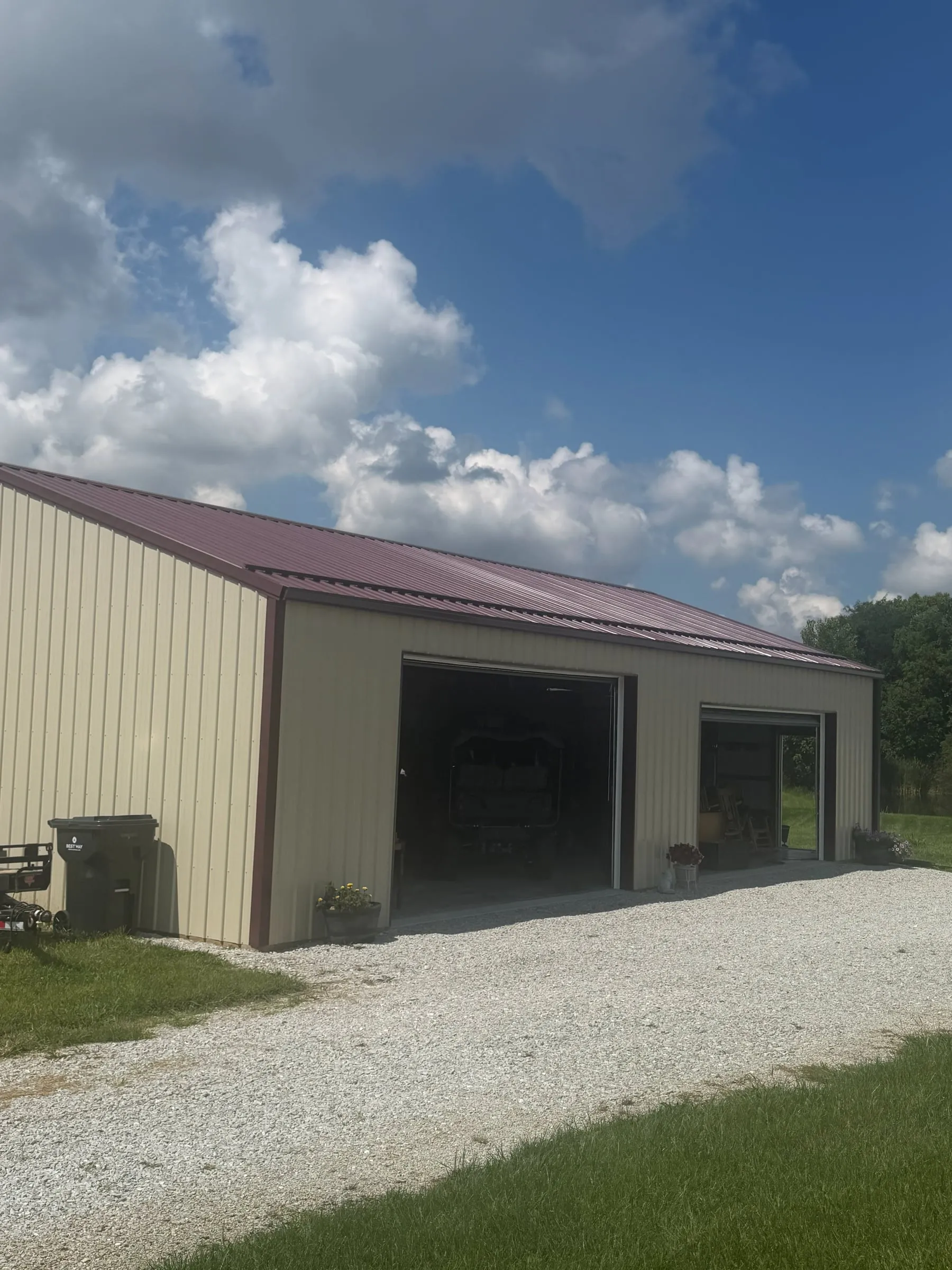 Tan shop with a brown roof and an overhead door on the gable end beside a gravel drive