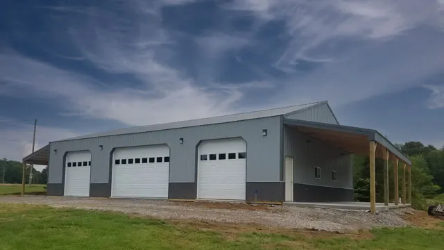 Gray post frame shop with three white overhead doors, charcoal wainscot and an open lean-to along one side