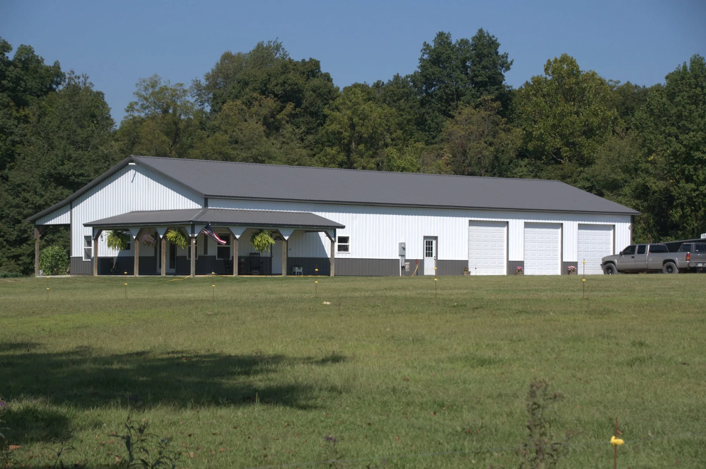 Long white building with a gray roof, a covered porch at one end and two overhead doors, with a car outside