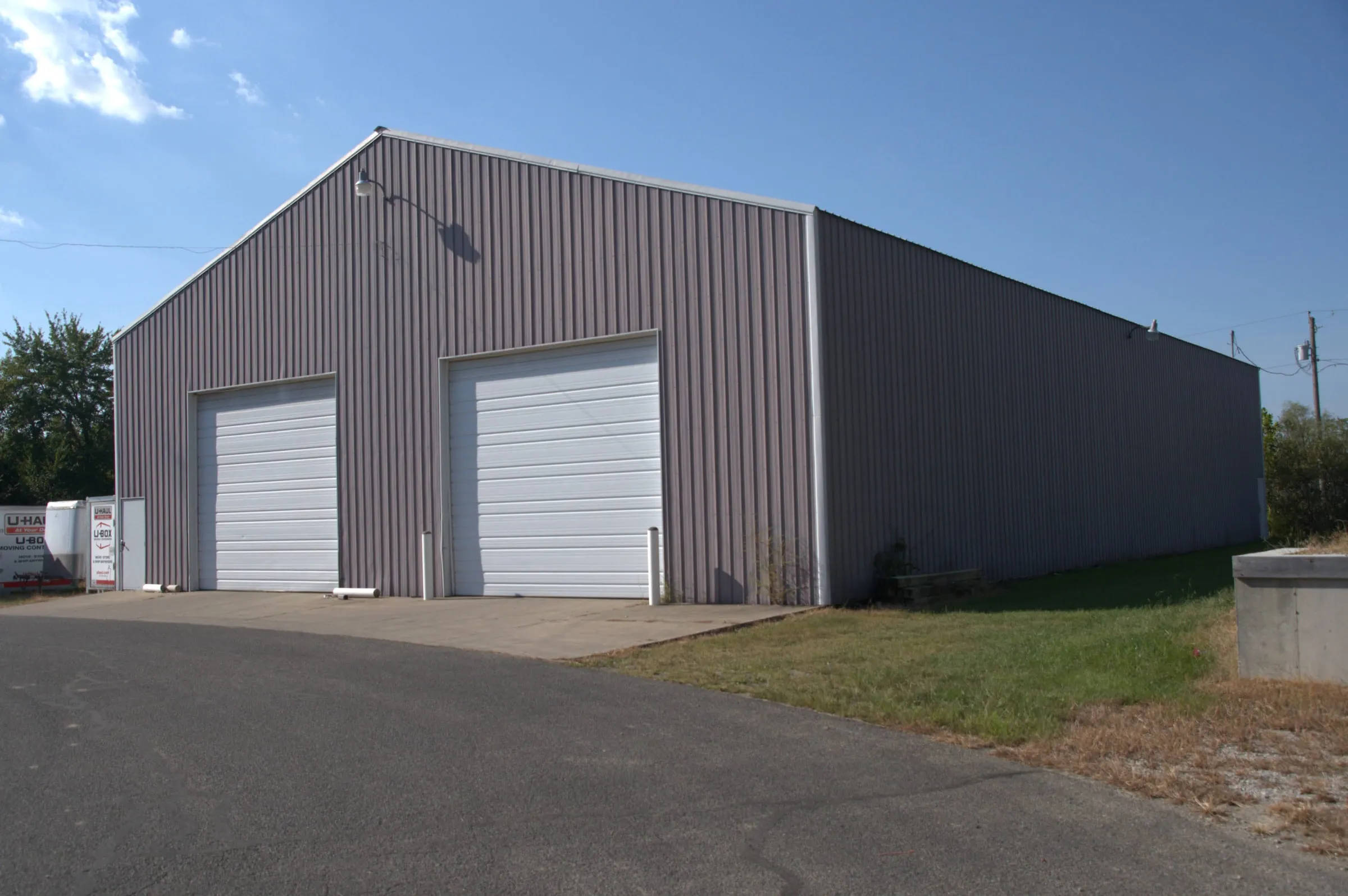 Gray shop with two white overhead doors on the gable end and a paved drive