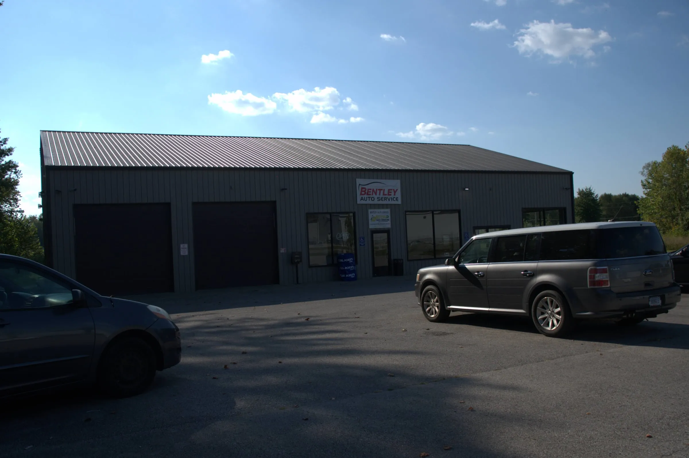 Charcoal commercial-style building with a brown roof, two dark overhead doors and cars parked out front