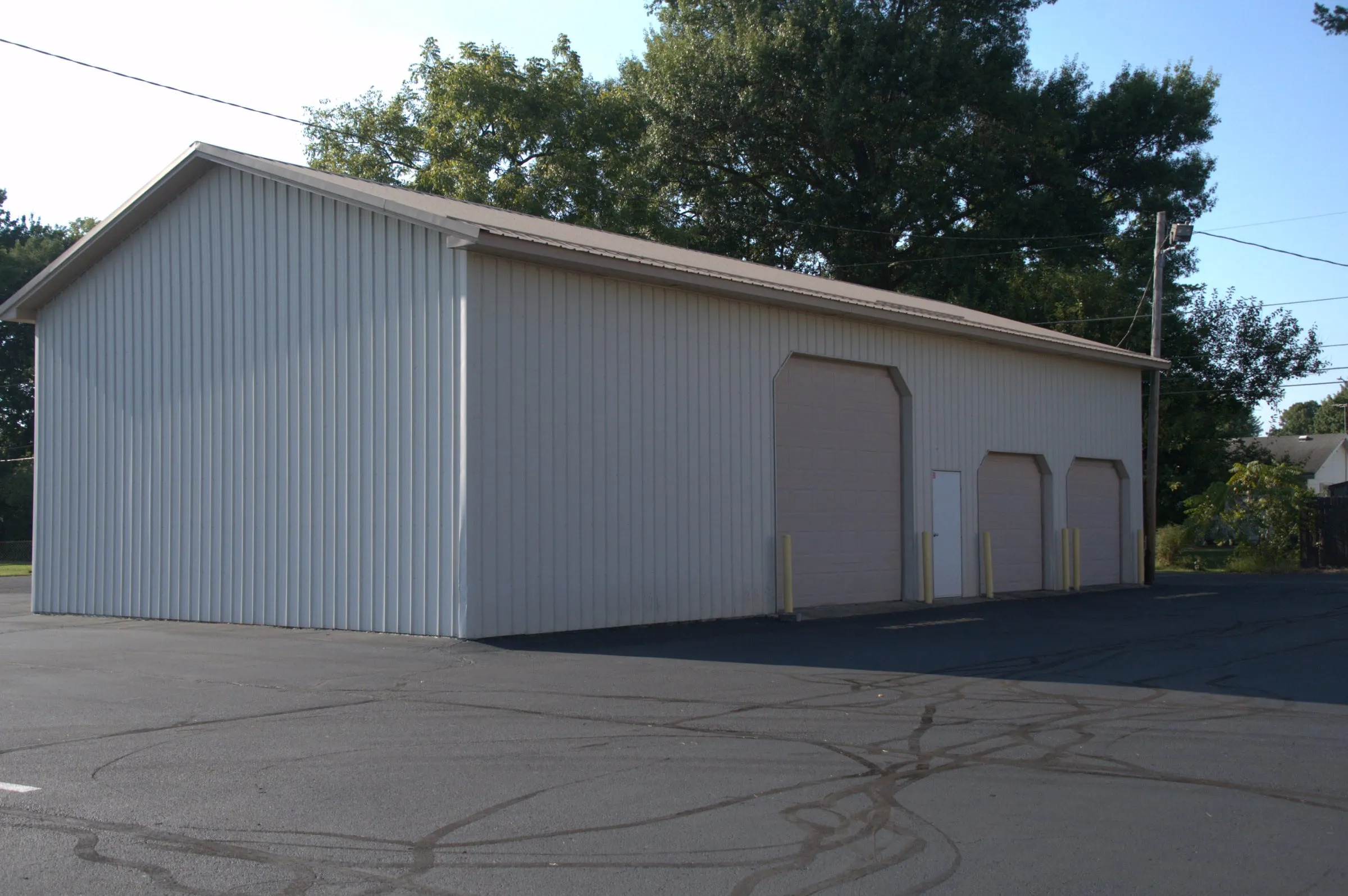 Light gray building with a dark roof, two overhead doors and a wide gable-end door on a paved lot
