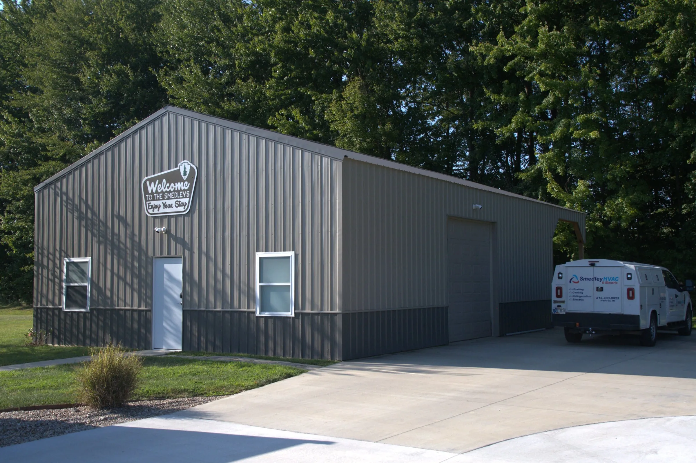 Gray building with a walk door, two windows and an end overhead door, white van parked on the concrete
