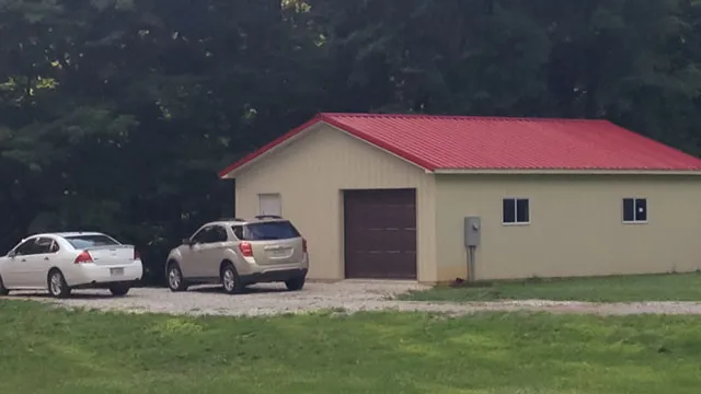 Cream building with a red roof and a brown overhead door, two cars on the drive