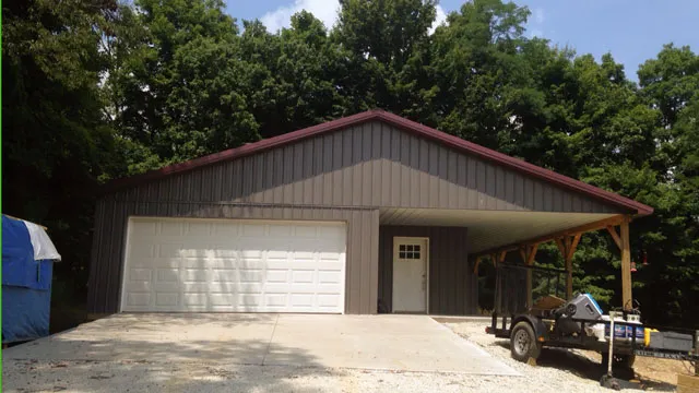 Tan garage with a maroon roof, a wide white overhead door and an open carport alongside