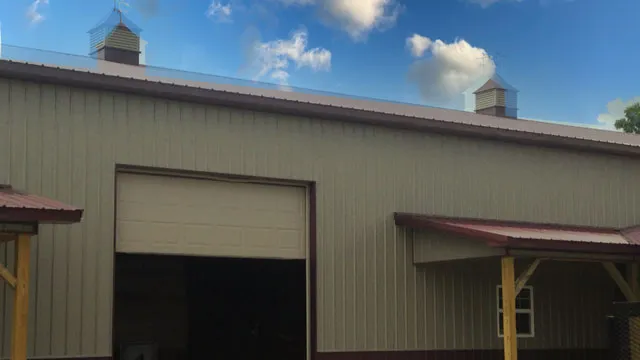 Tan building with a tall open bay, an overhead door, two small shed roofs and a cupola on the ridge