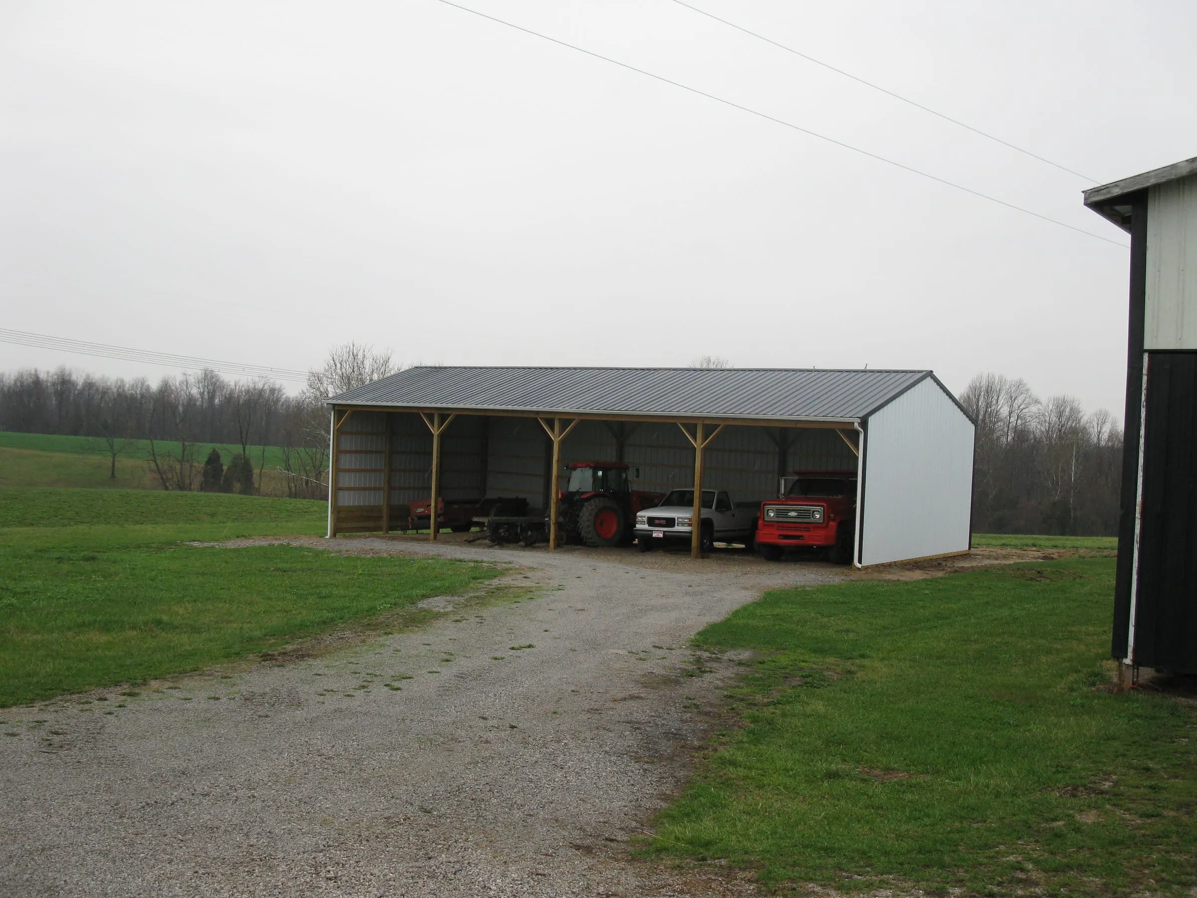 Open-front pole shed on timber posts with a gray roof, tractor and car parked under it