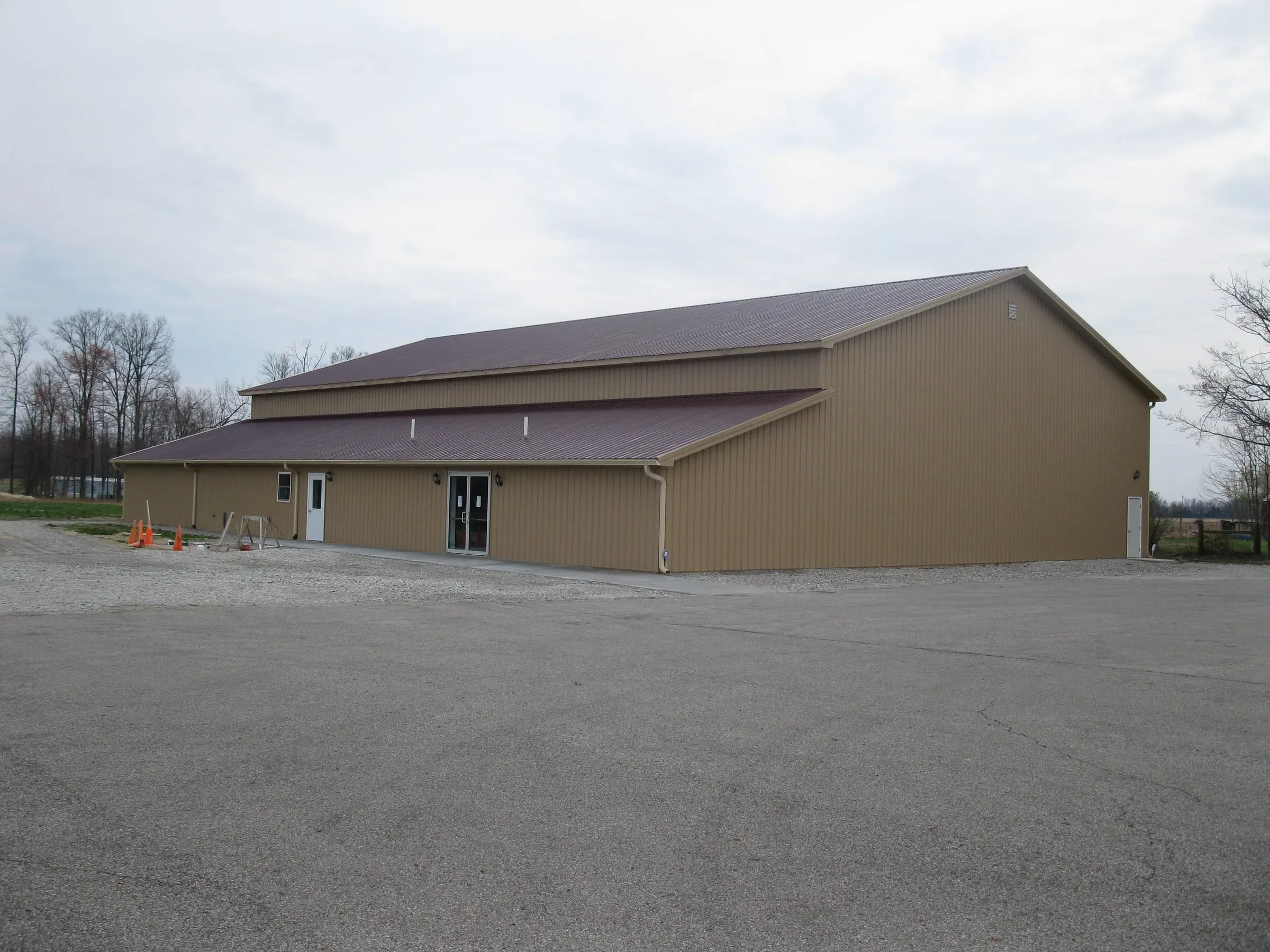 Tan commercial building with a maroon roof and a lean-to along the front, on a paved lot