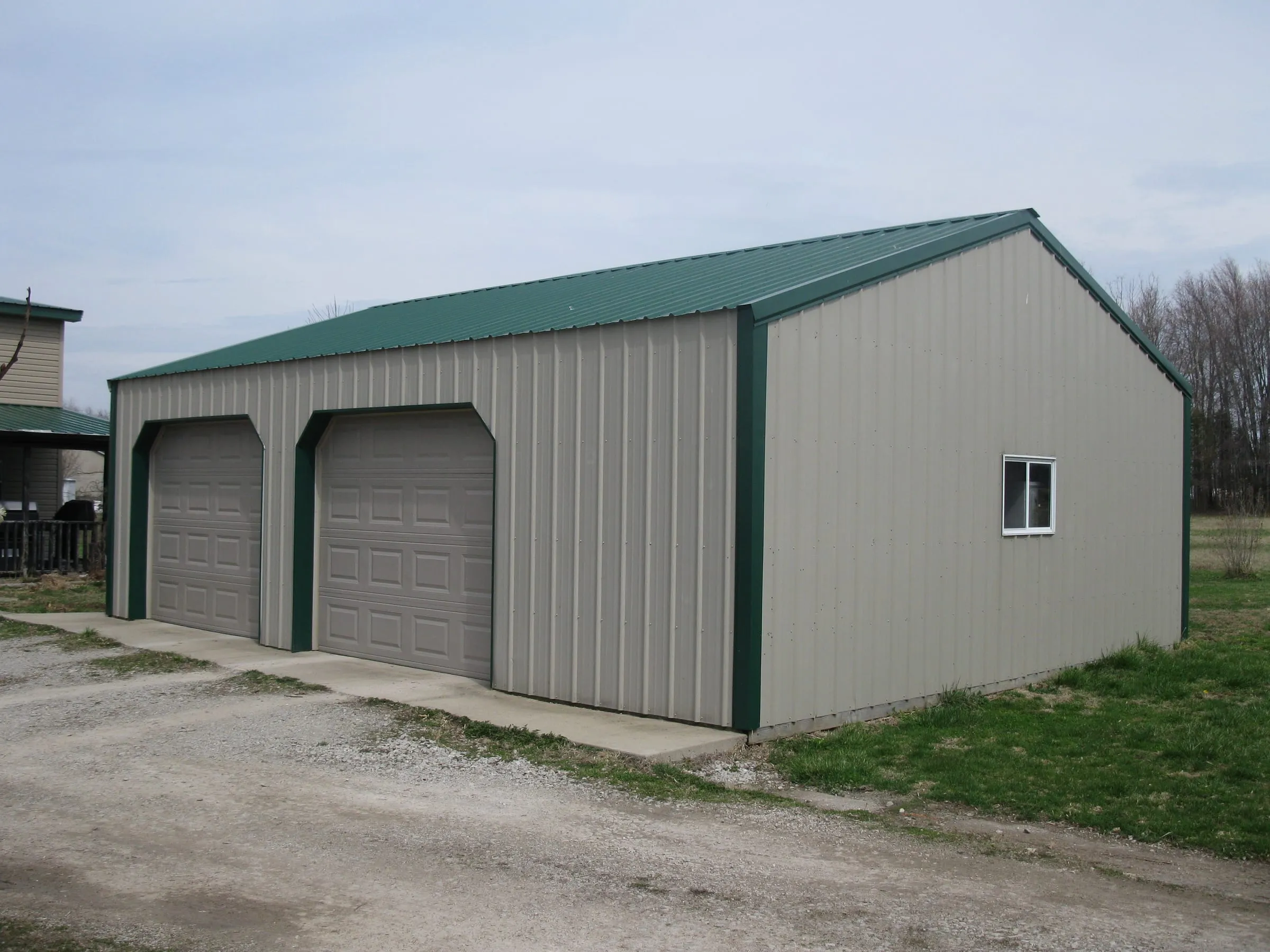 Cream shop with a green roof and green trim and two overhead doors on a concrete drive