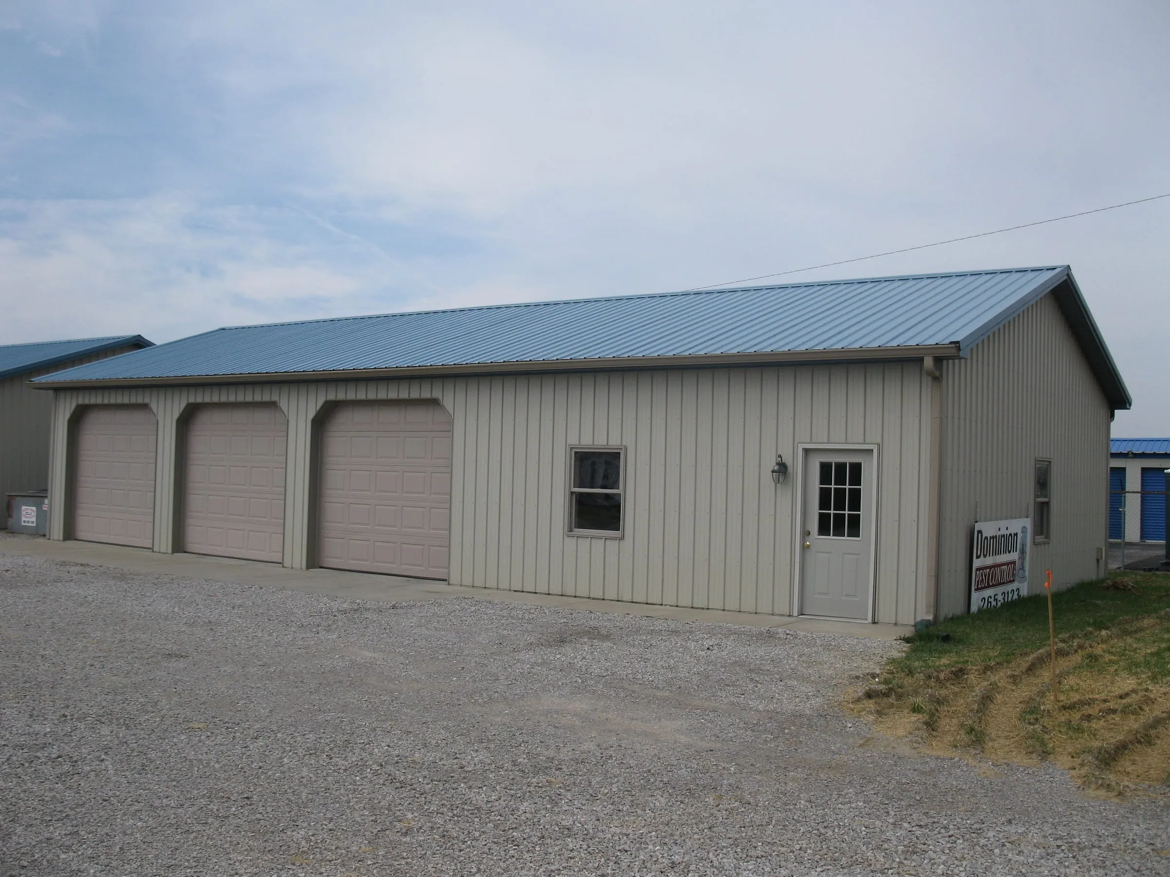 Cream commercial building with a blue roof, three overhead doors, a walk door and signage