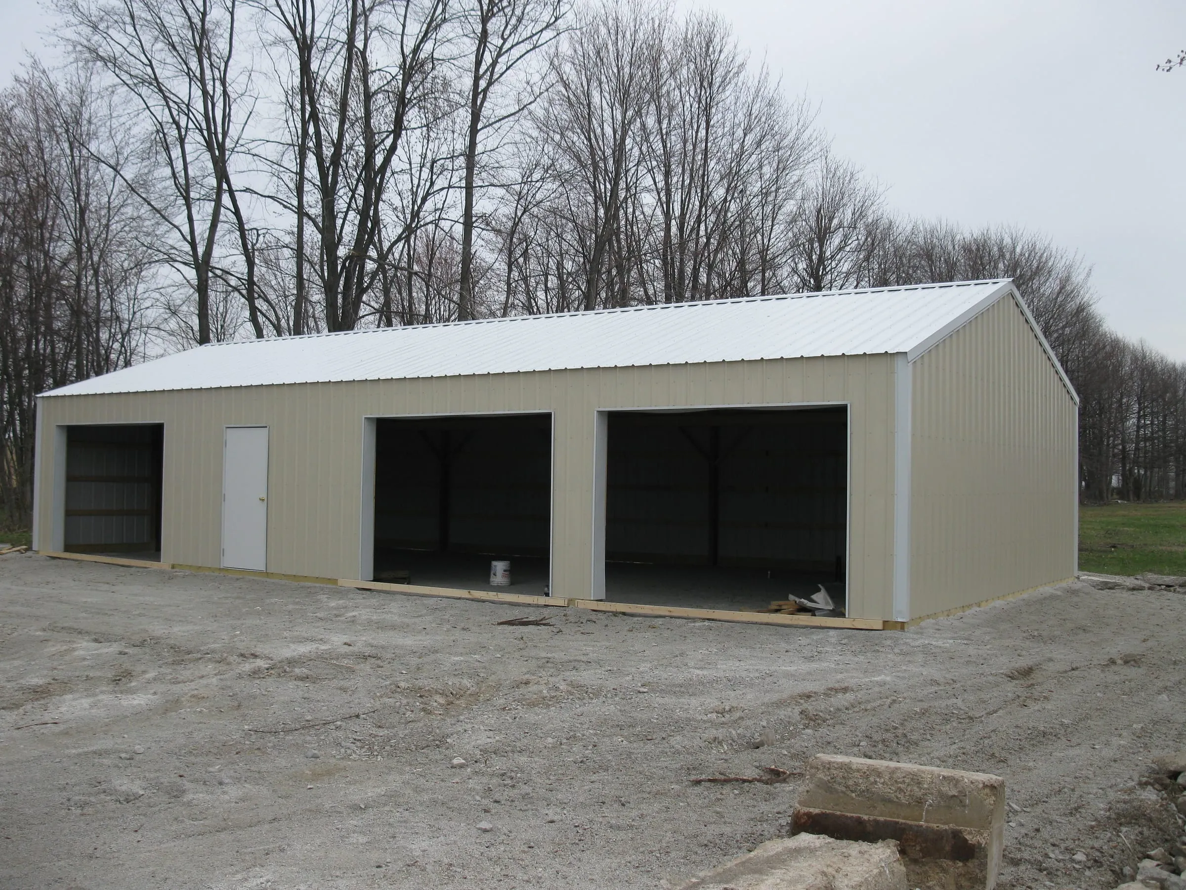 Cream building with a white roof and three open bays on a gravel pad