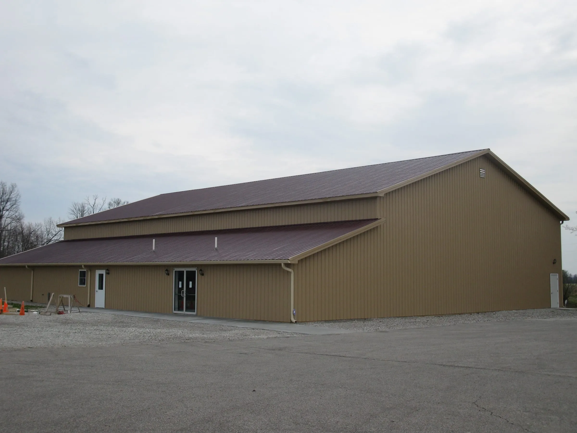 Tan commercial building with a maroon roof and a covered lean-to, paved parking in front