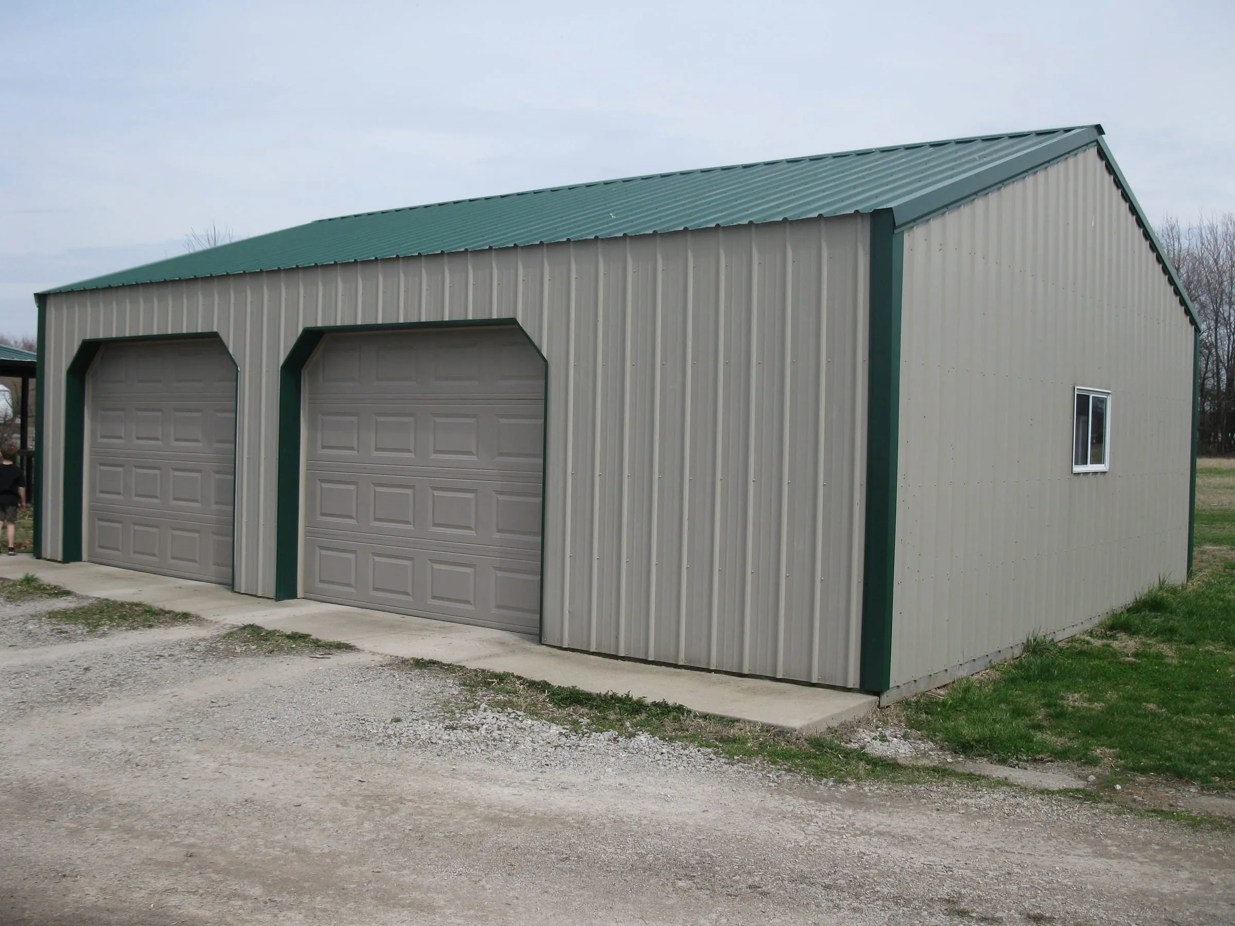 Cream shop with a green roof and green corner trim, two overhead doors and a side window