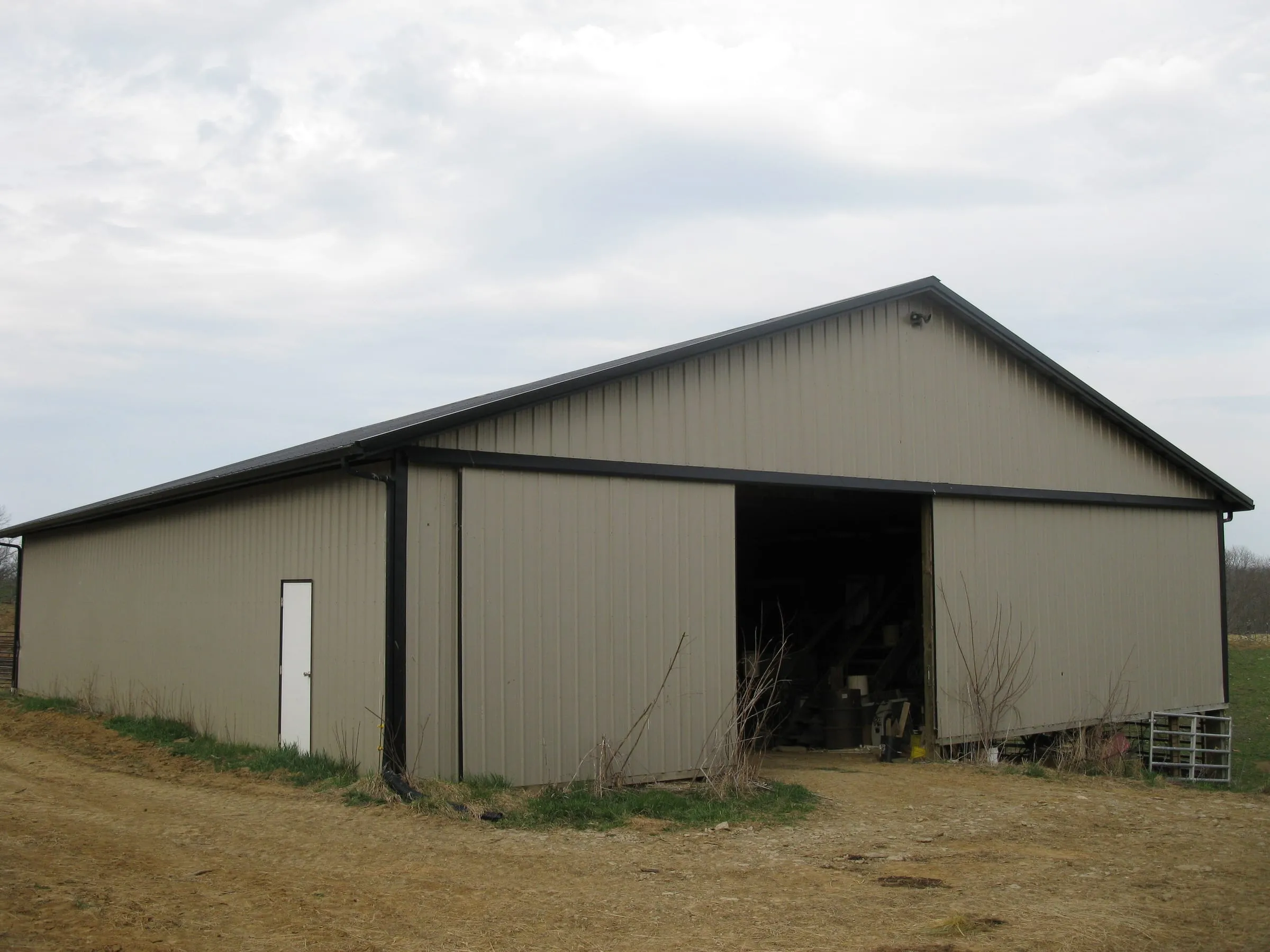 Tan barn with a wide open bay in the gable end, standing in winter grass