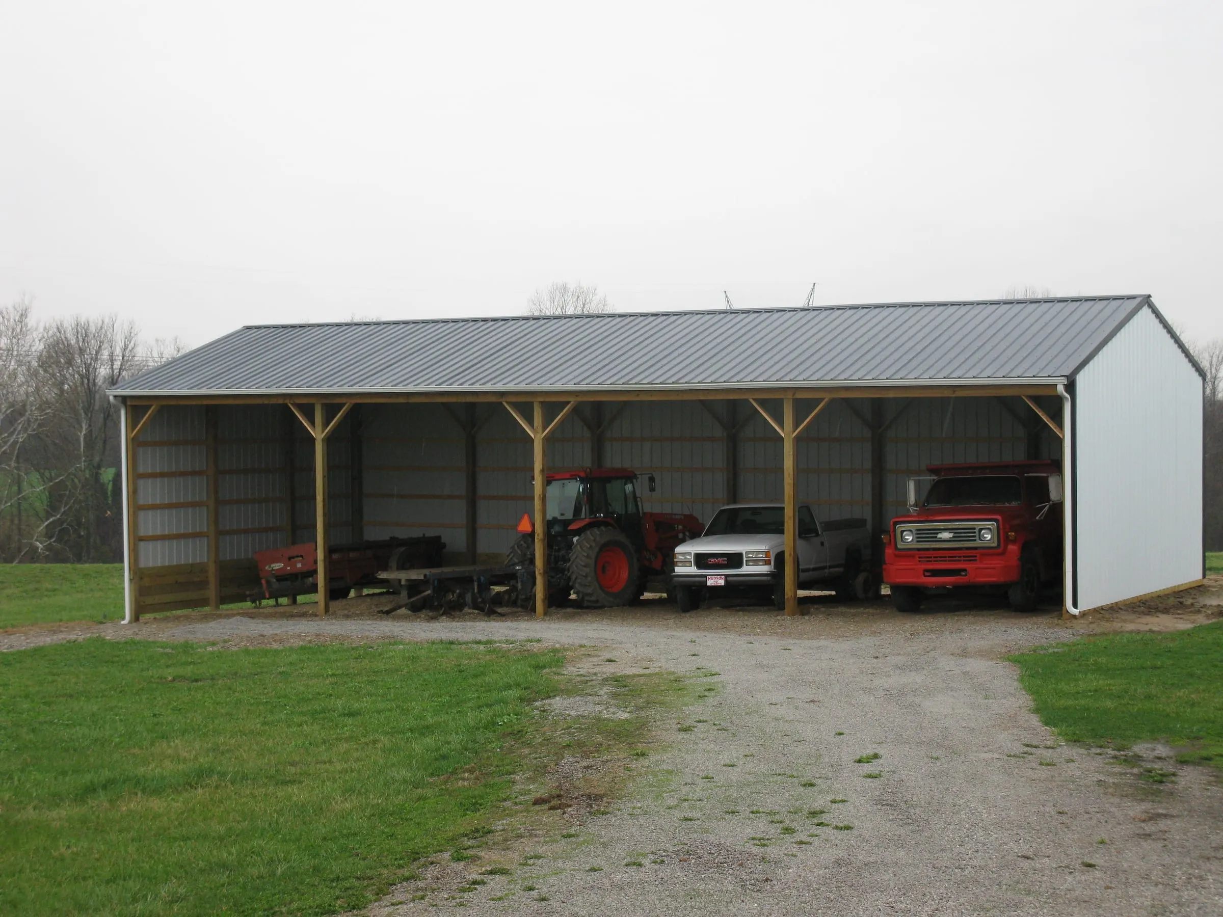 Open-front pole shed with timber posts sheltering a tractor and a car