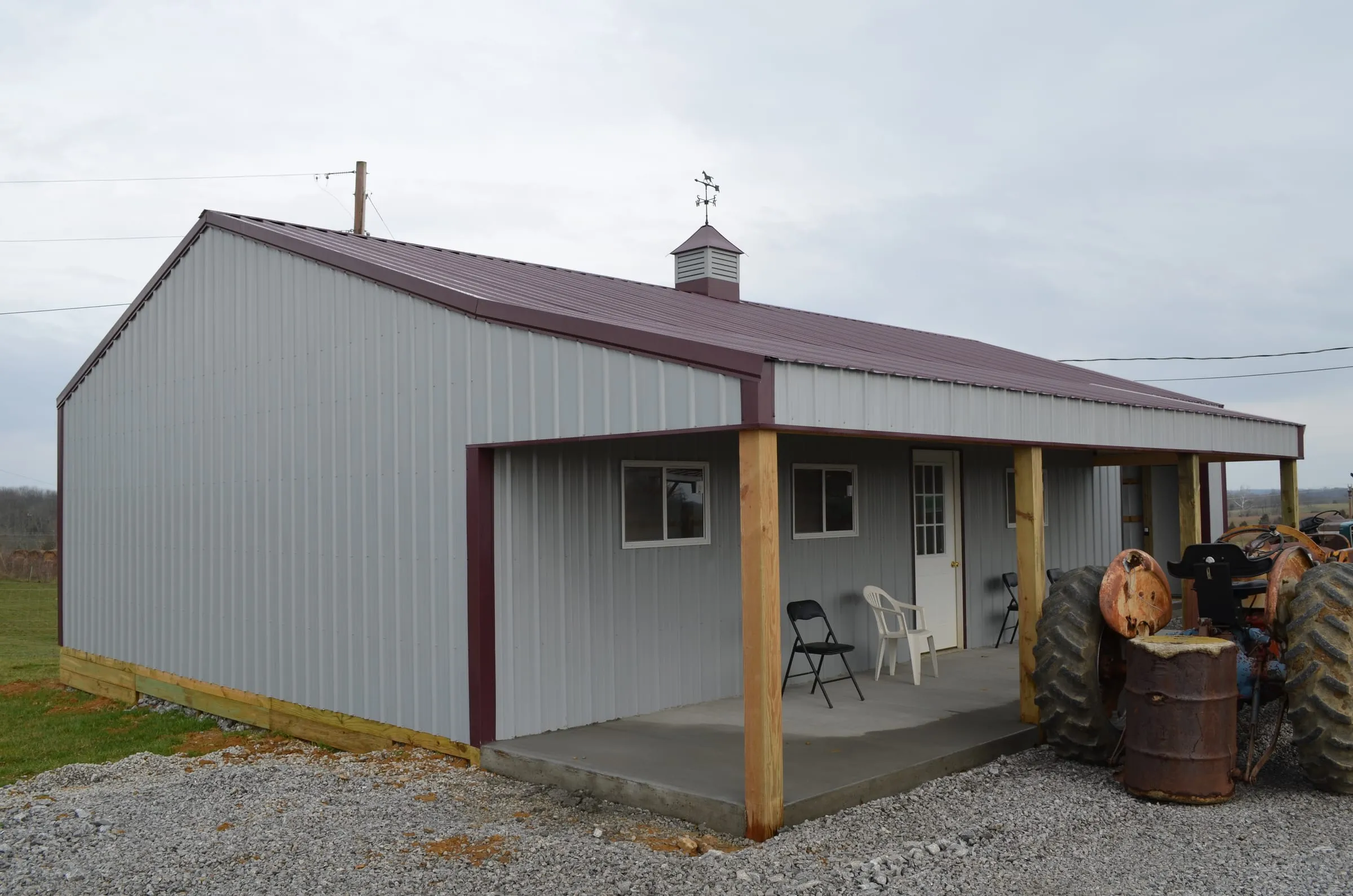 Gray shop with a maroon roof and trim, a timber-post porch and a cupola on the ridge