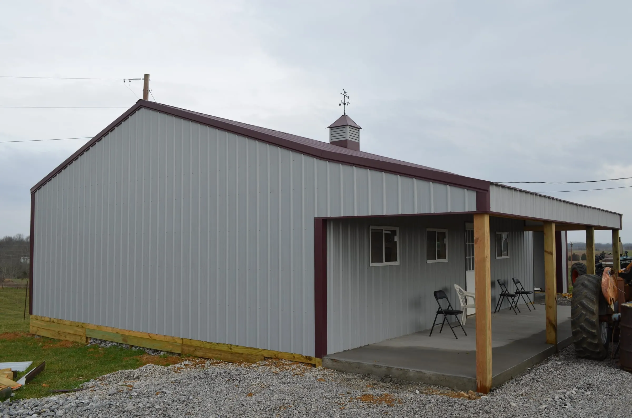 Gray building with a maroon roof and a timber-post porch with chairs under it