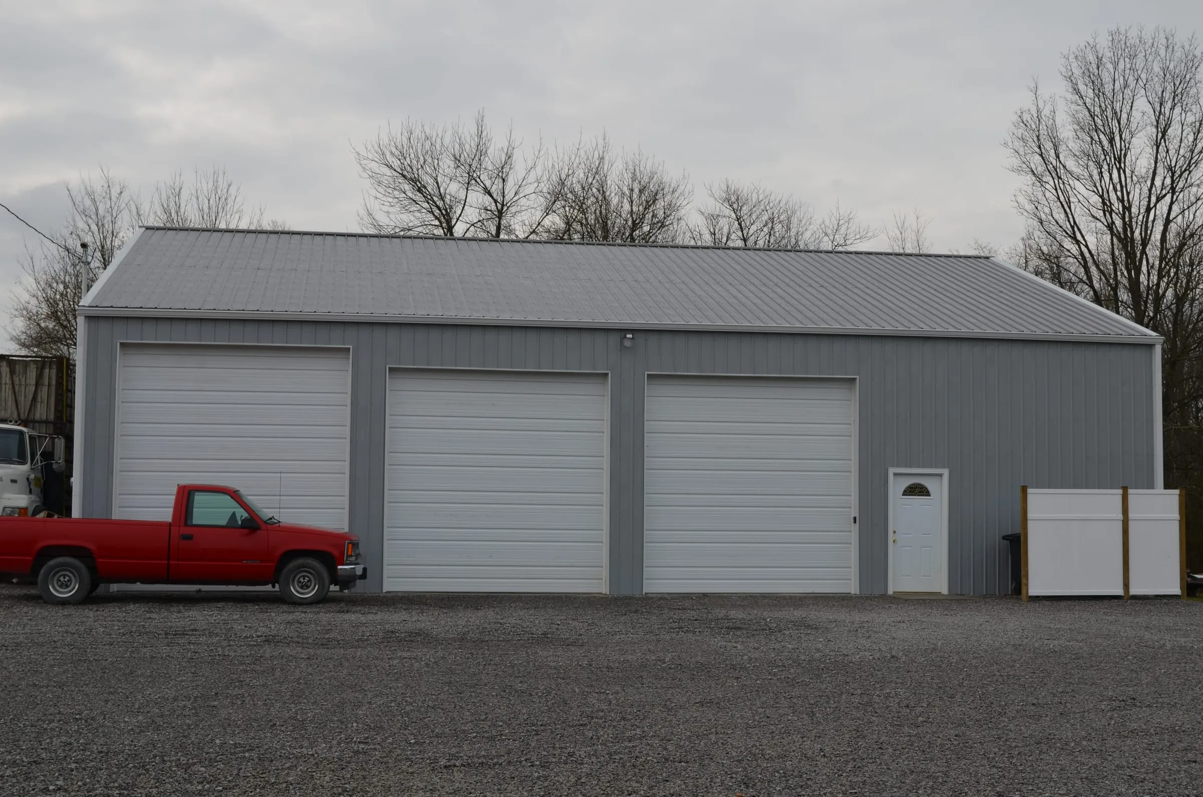 Gray building with three white overhead doors, red pickup parked in front