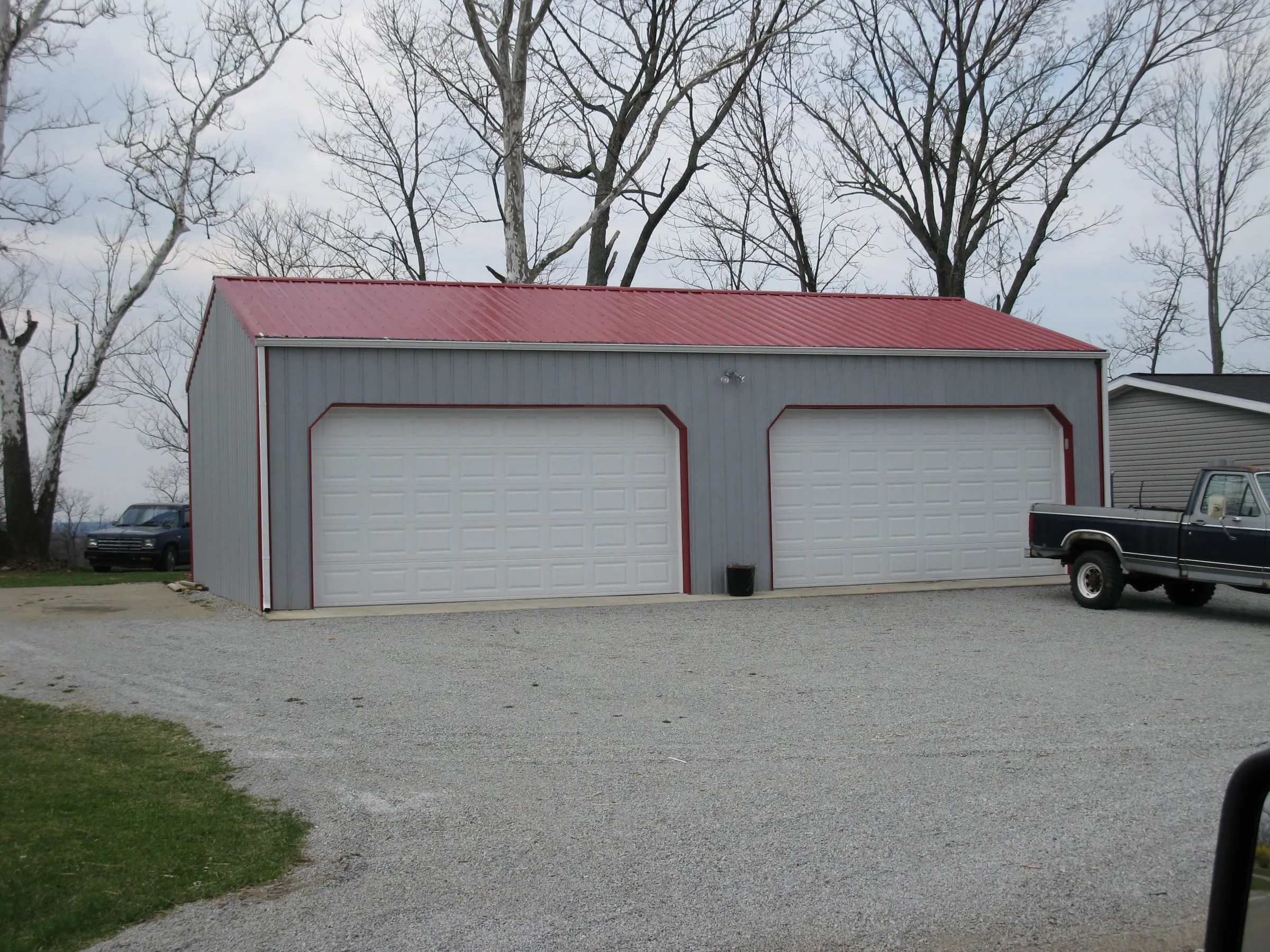 Cream building with a maroon roof and two white overhead doors, pickup parked alongside