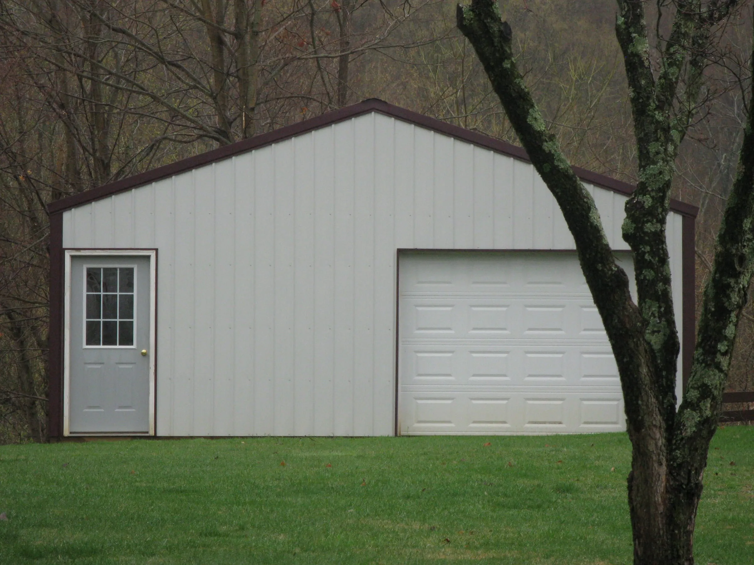 Cream building with a white walk door and a white overhead door, tree in the foreground