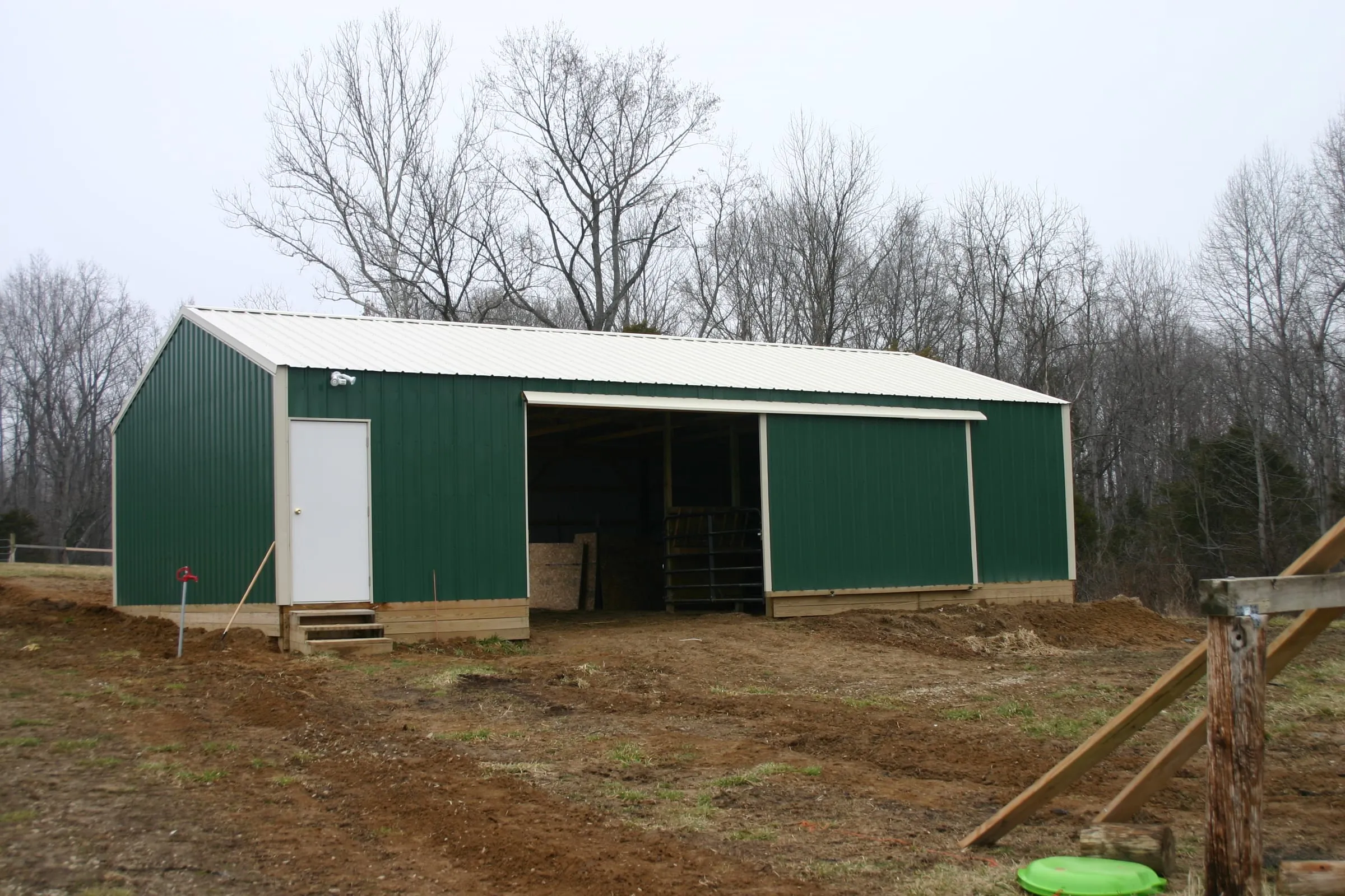 Green barn with a white roof and trim, a walk door and an open bay between sliding doors