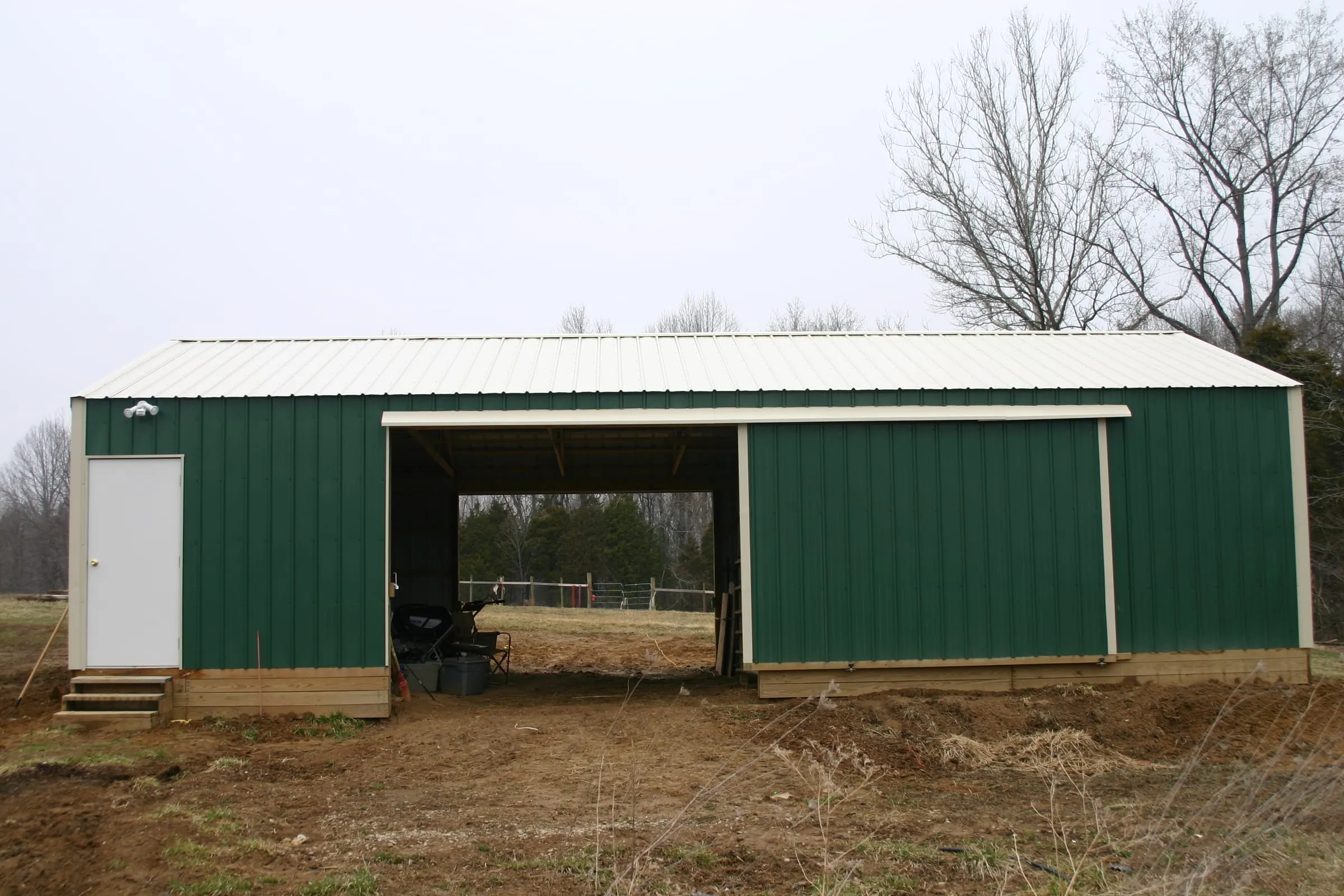 Green barn with a white roof and a wide open bay, ground still bare
