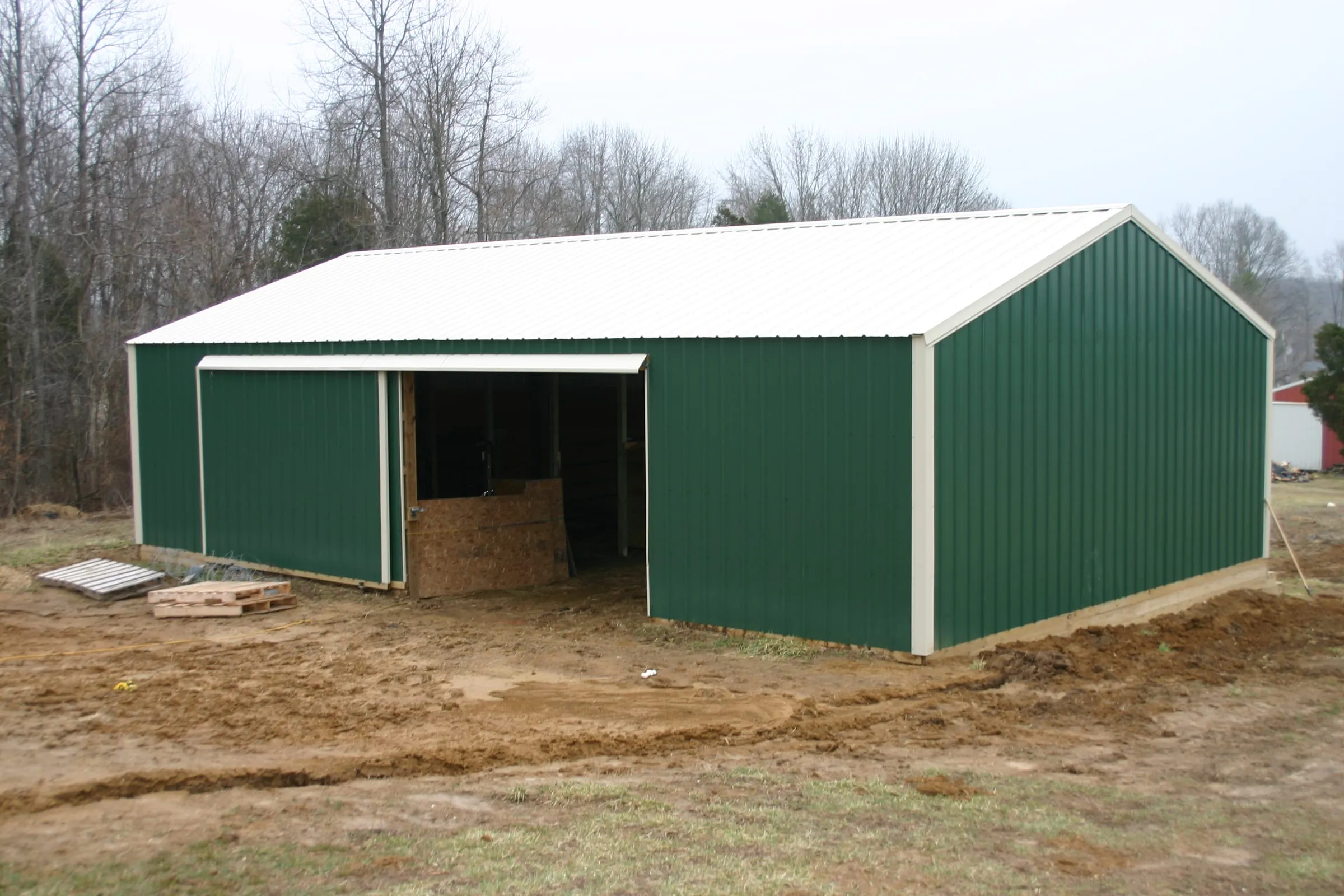 Green barn with a white roof and an open bay with hay stored inside