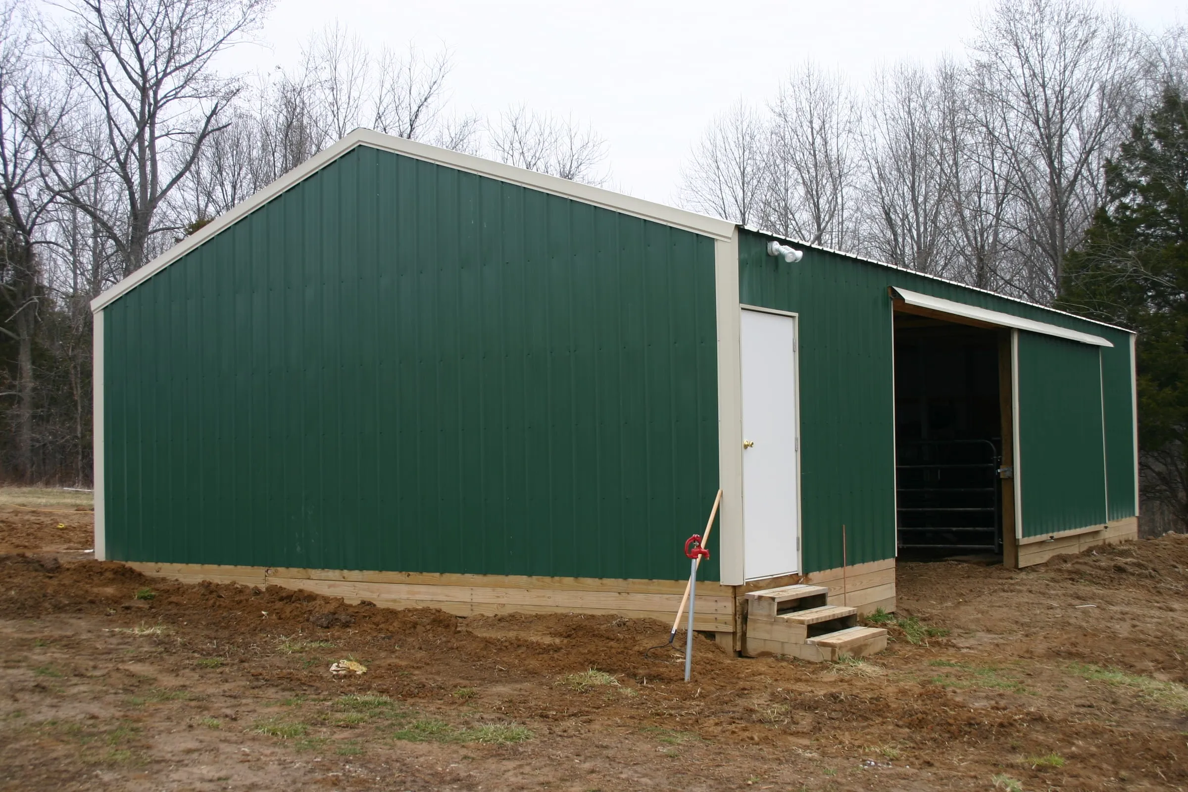 Green barn with a white roof and trim, a walk door with steps and an open bay