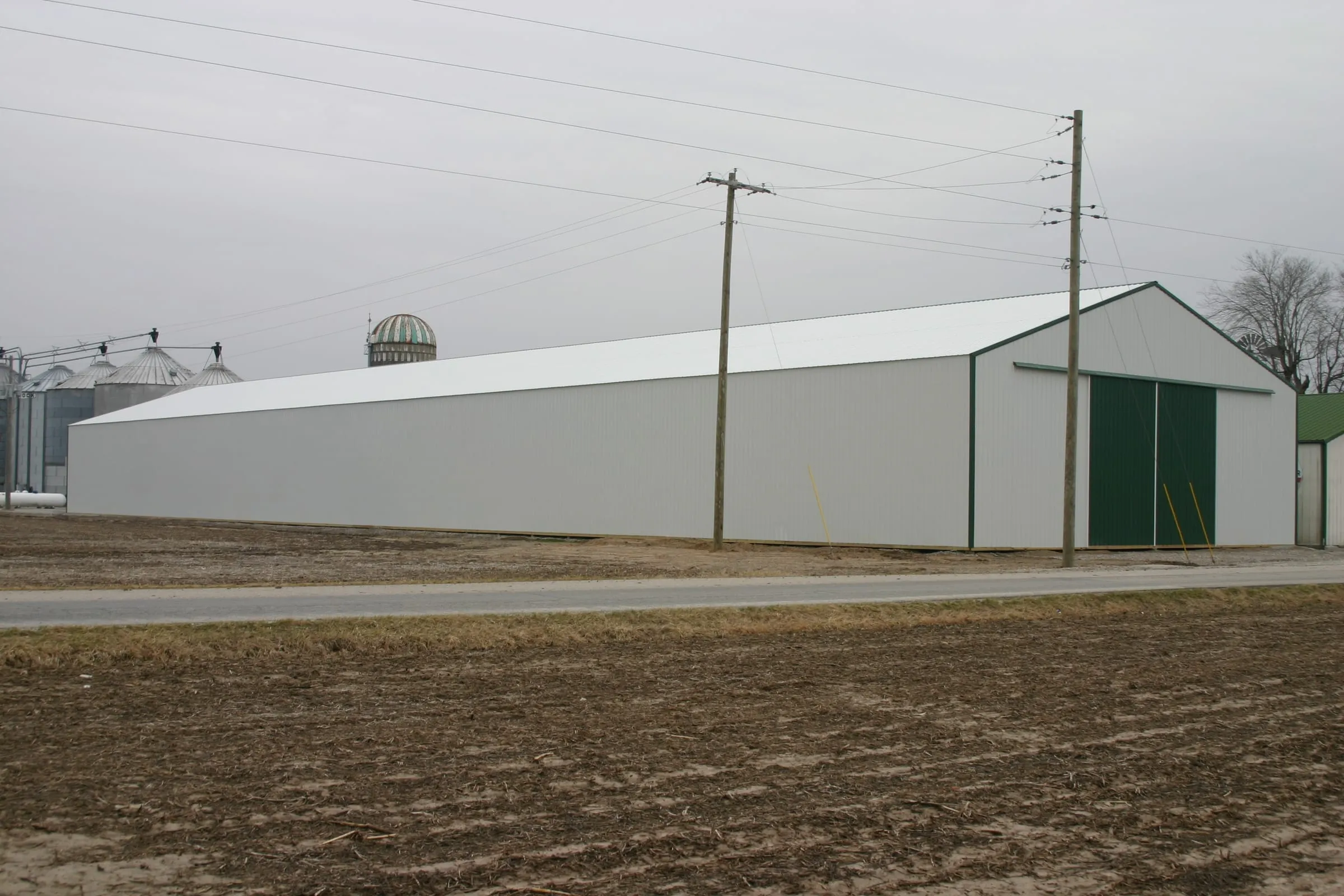 Long white machine shed running away down the field edge, green door at the near end