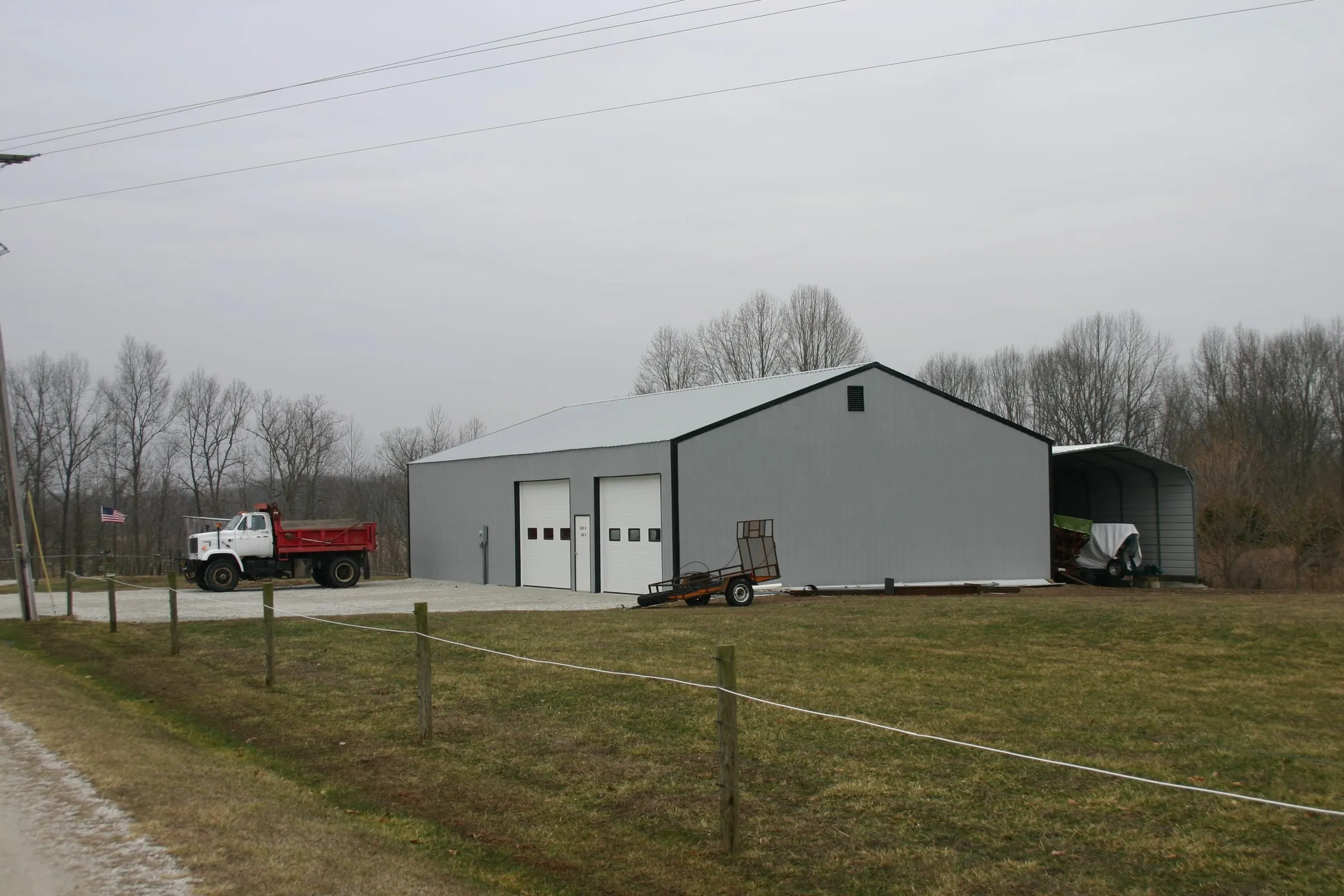 White commercial building with an open lean-to, dump truck and trailer parked alongside