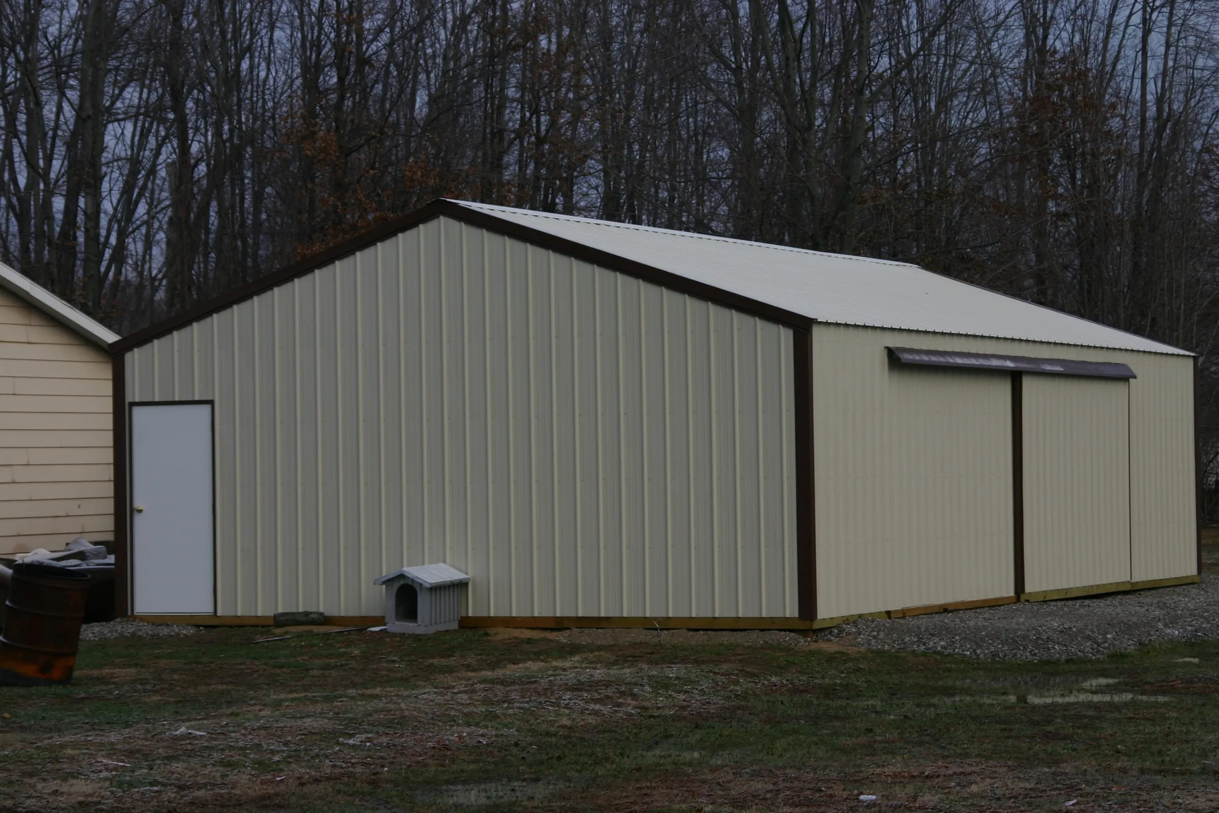 Cream building with brown trim, a walk door and sliding doors, dog kennel alongside